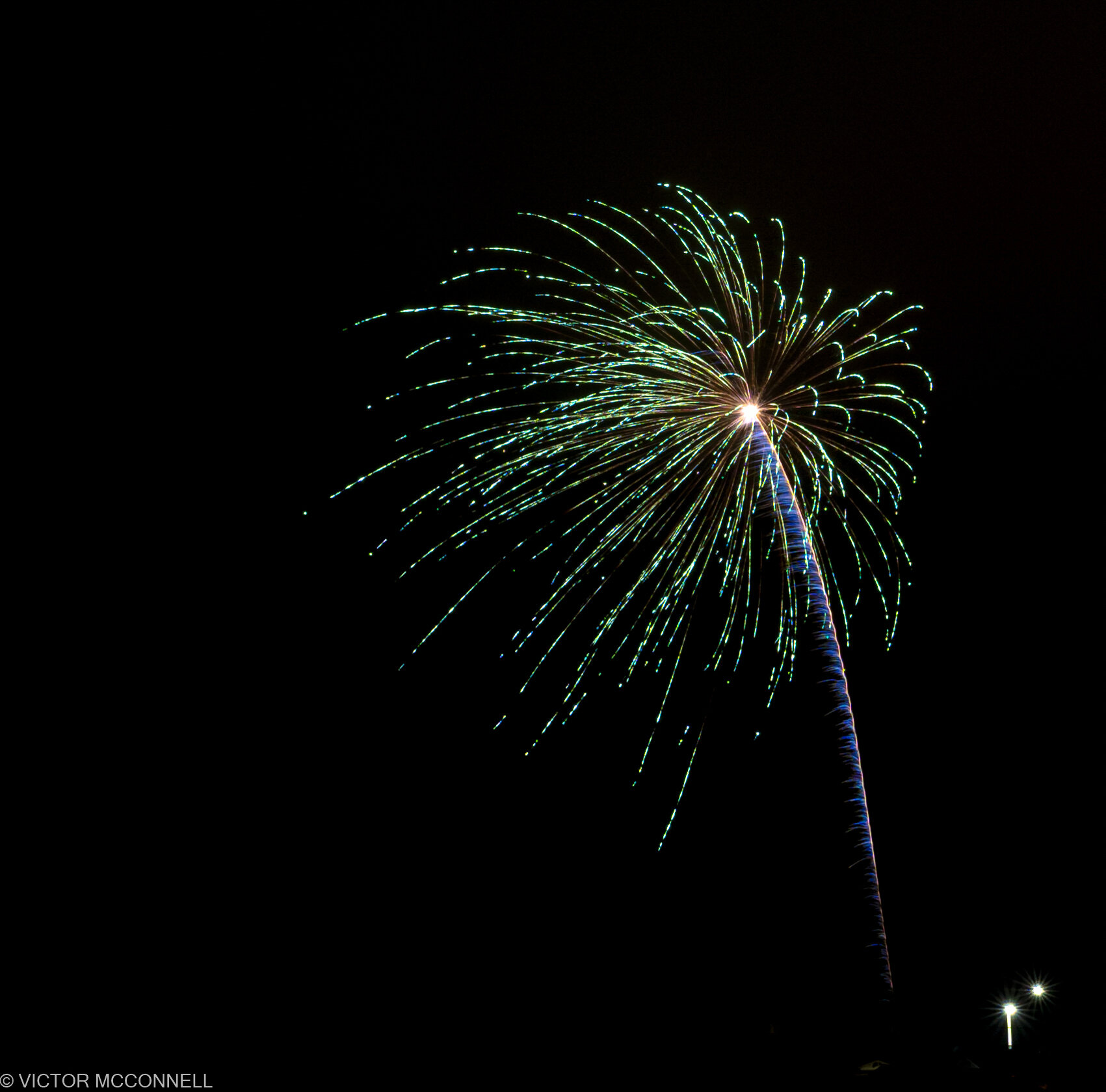 Colorful fireworks exploding in the night sky with streaks of green, purple, and yellow light radiating outward.