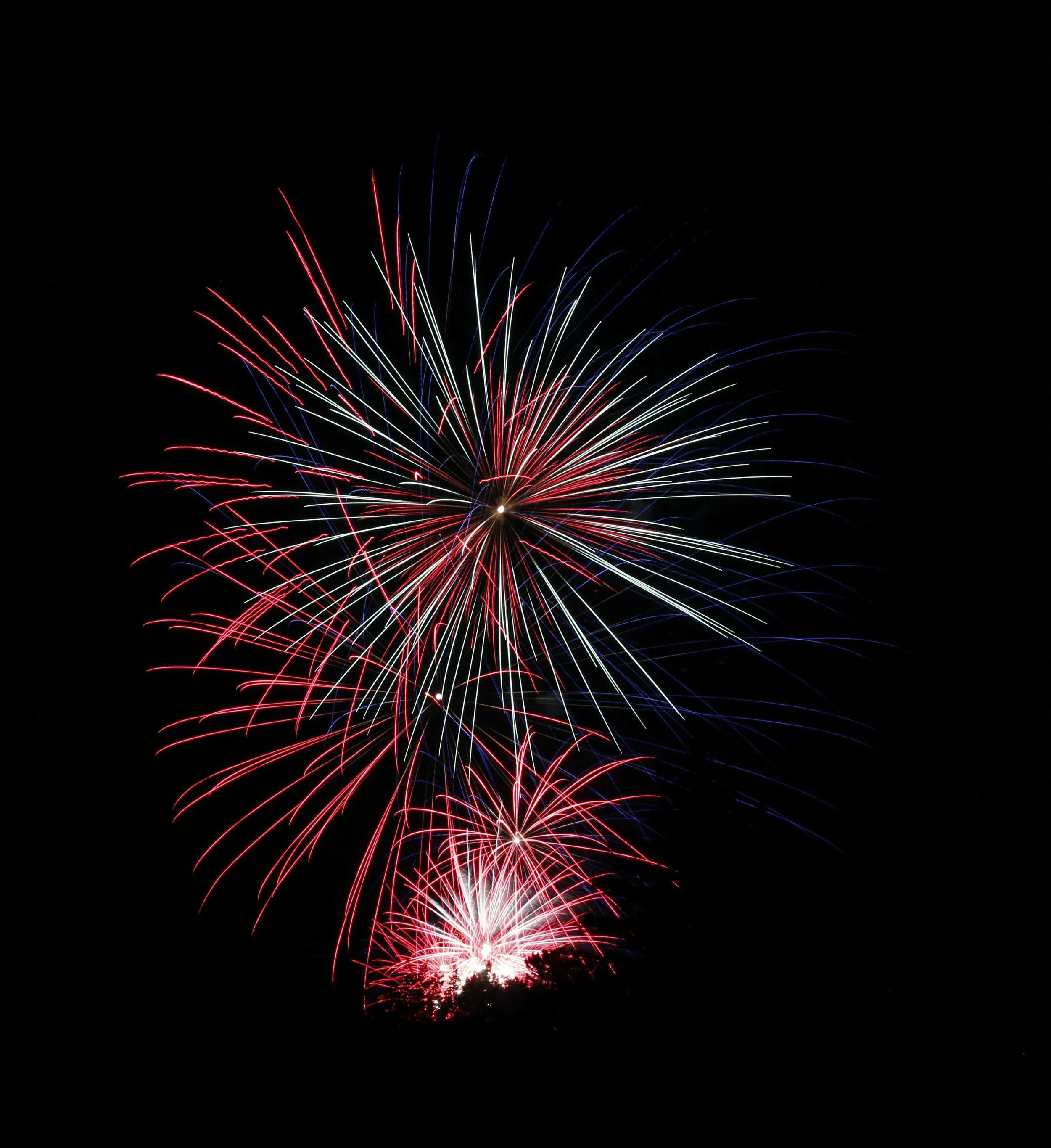 Fireworks display with red, white, and blue streaks exploding against a dark night sky for a celebration.