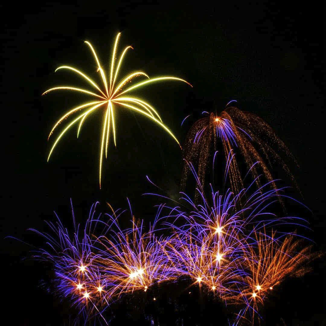 Colorful fireworks display in the night sky with bursts of yellow, purple, and orange lights.