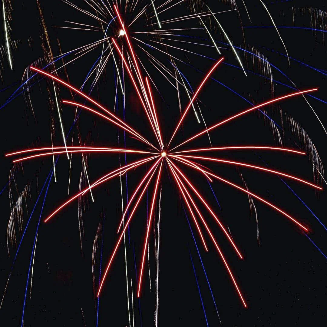 Colorful fireworks exploding in a night sky with red, white, and blue streaks of light radiating outward.
