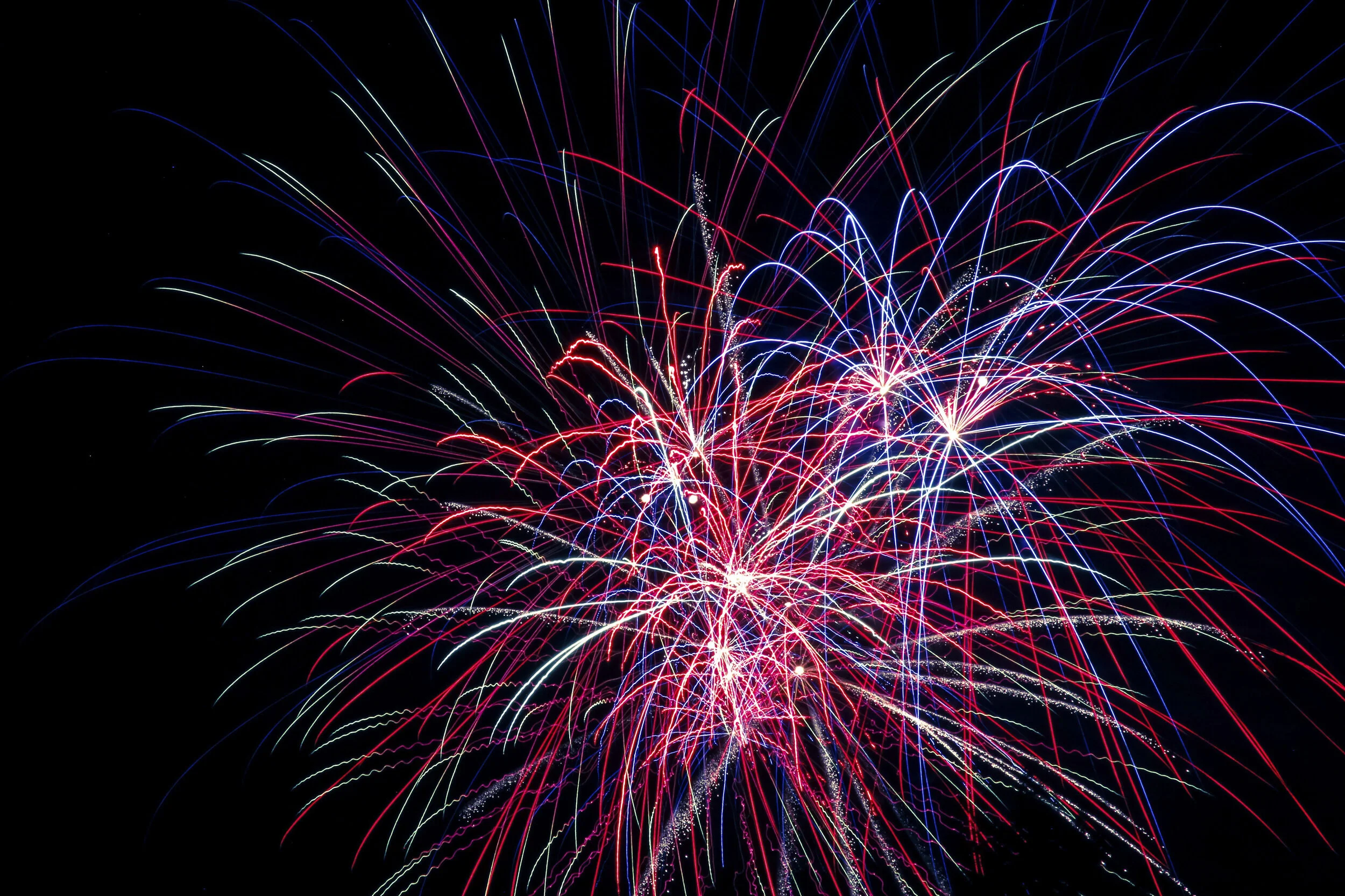 Colorful fireworks bursting against a black sky, with streaks of red, white, blue, and purple light.