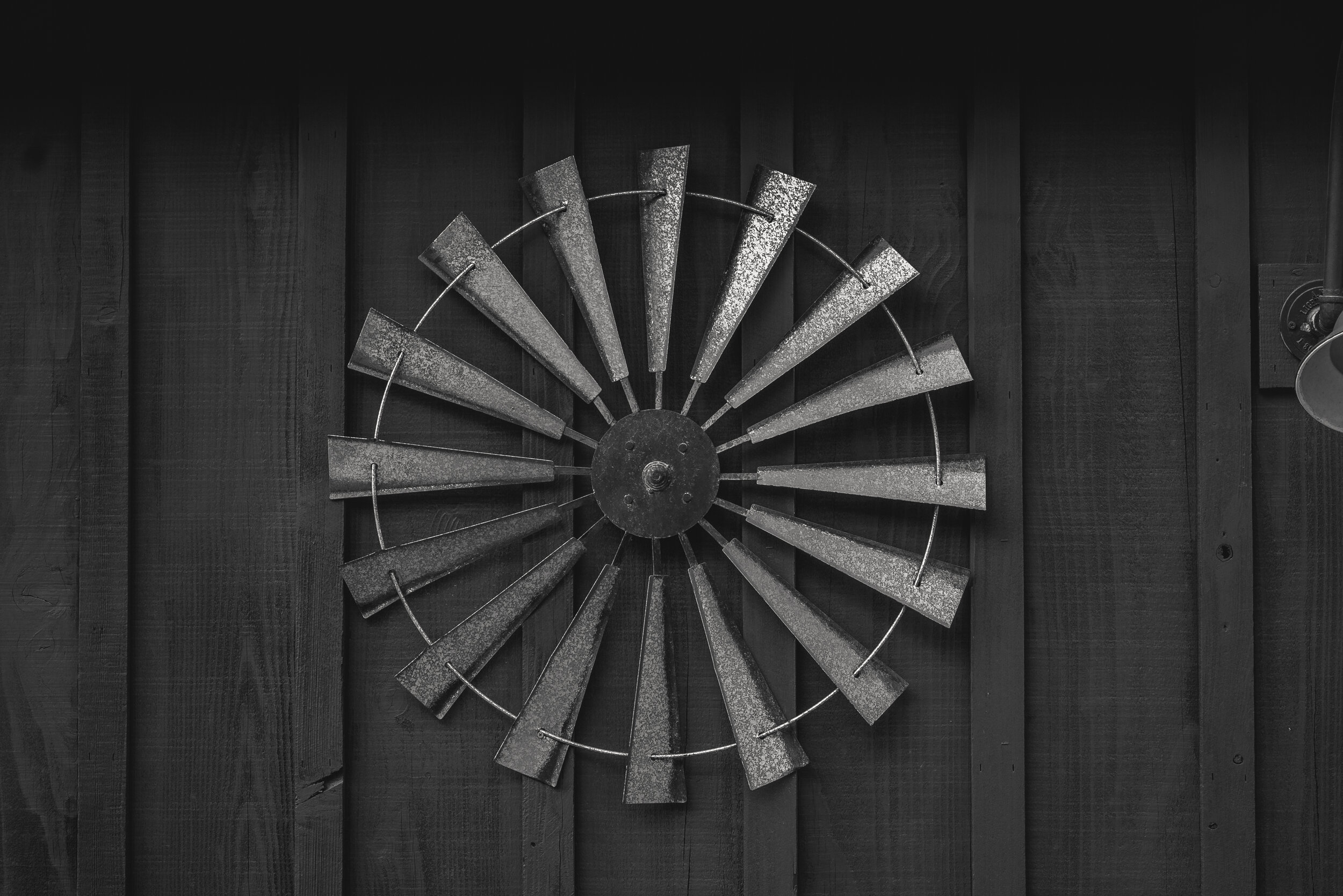 A metal windmill sculpture mounted on a dark wooden wall.