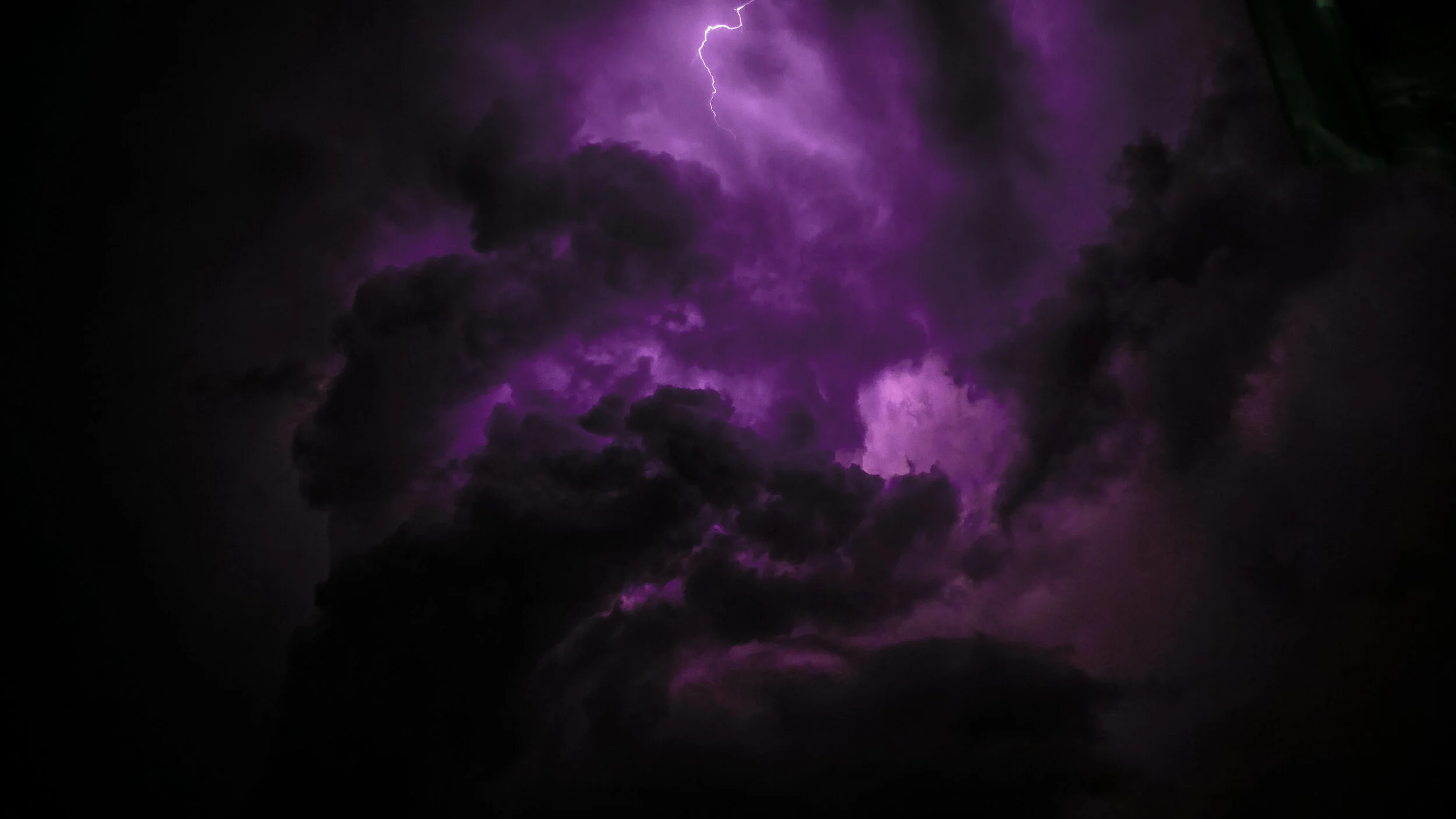 Purple lightning bolt striking through dark storm clouds at night.