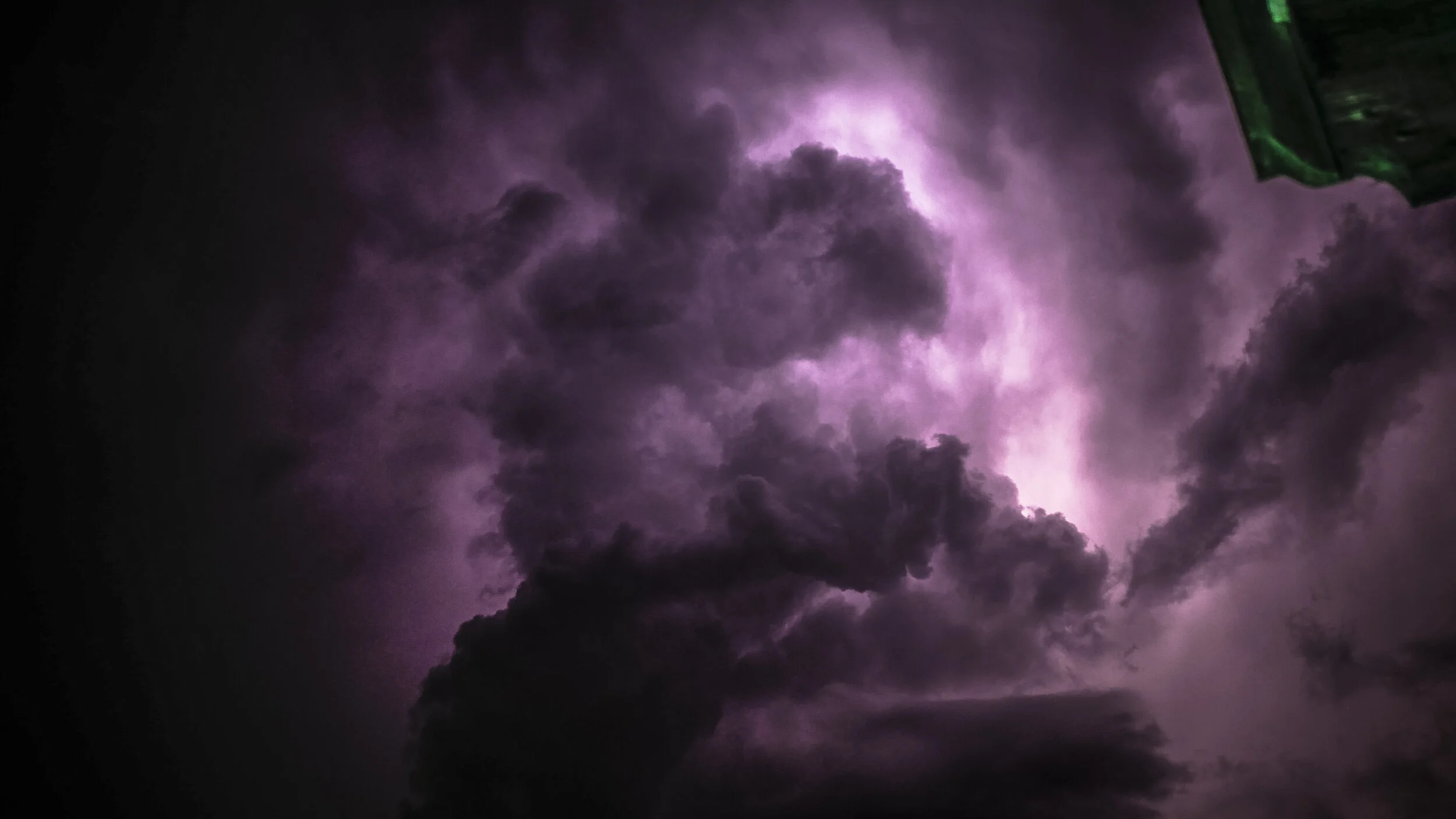 Dark storm clouds illuminated by purple lightning in the night sky.