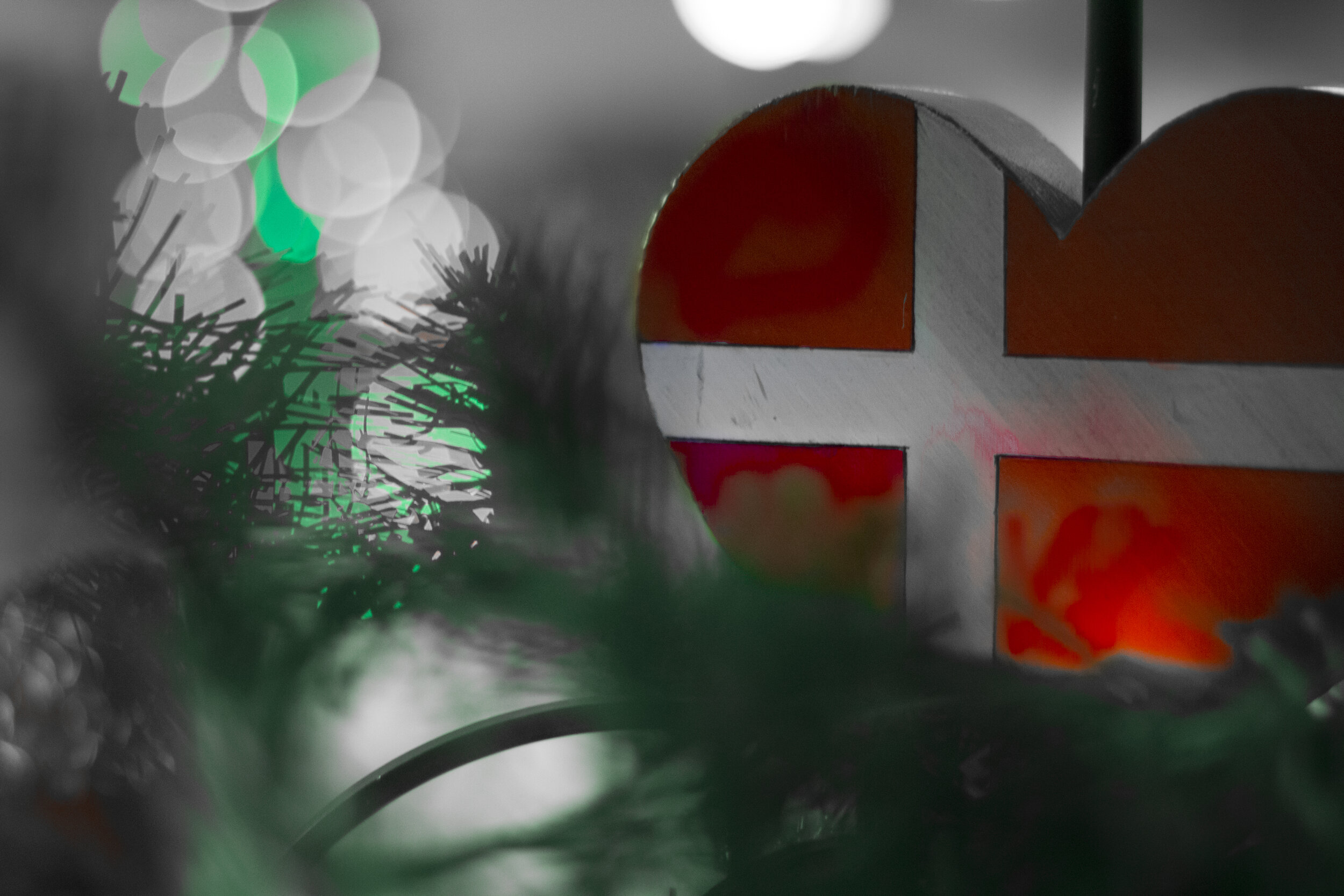 Close-up of a colorful, blurry Christmas decoration with green, white, and red elements, including a frosted Christmas tree branch and a large red and white striped object in the background.