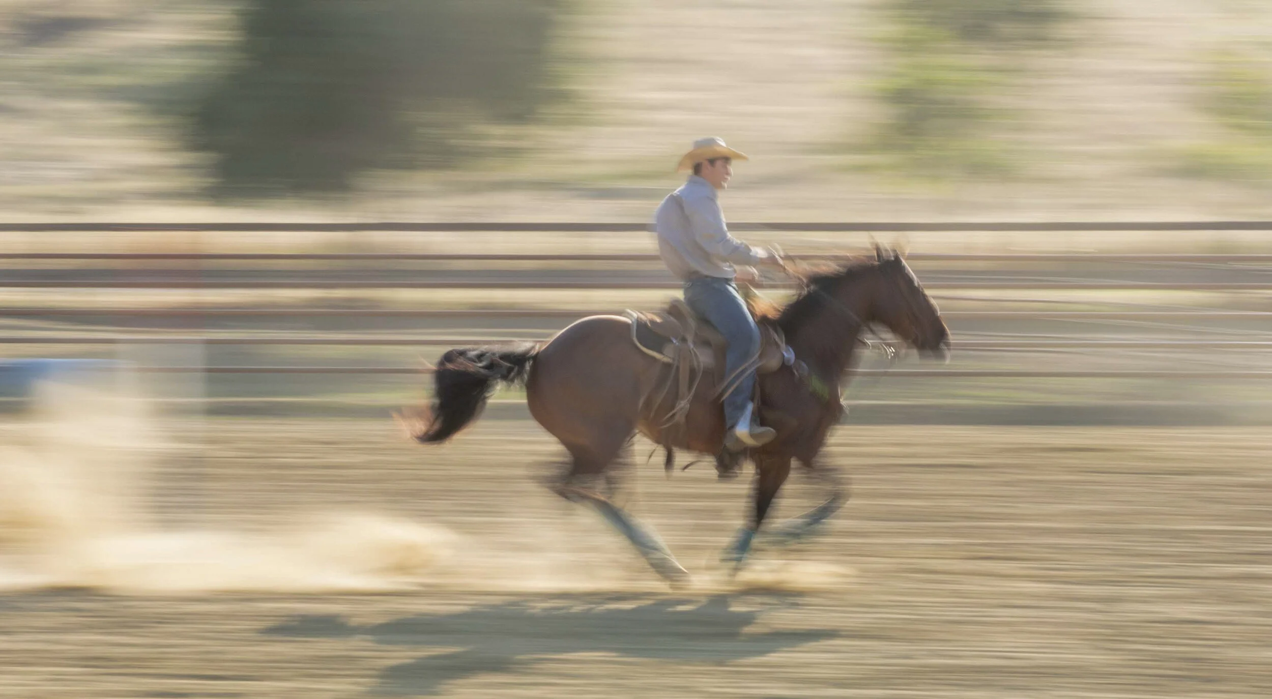 A person riding a horse at high speed on a dusty outdoor arena, with a motion blur background indicating fast movement.