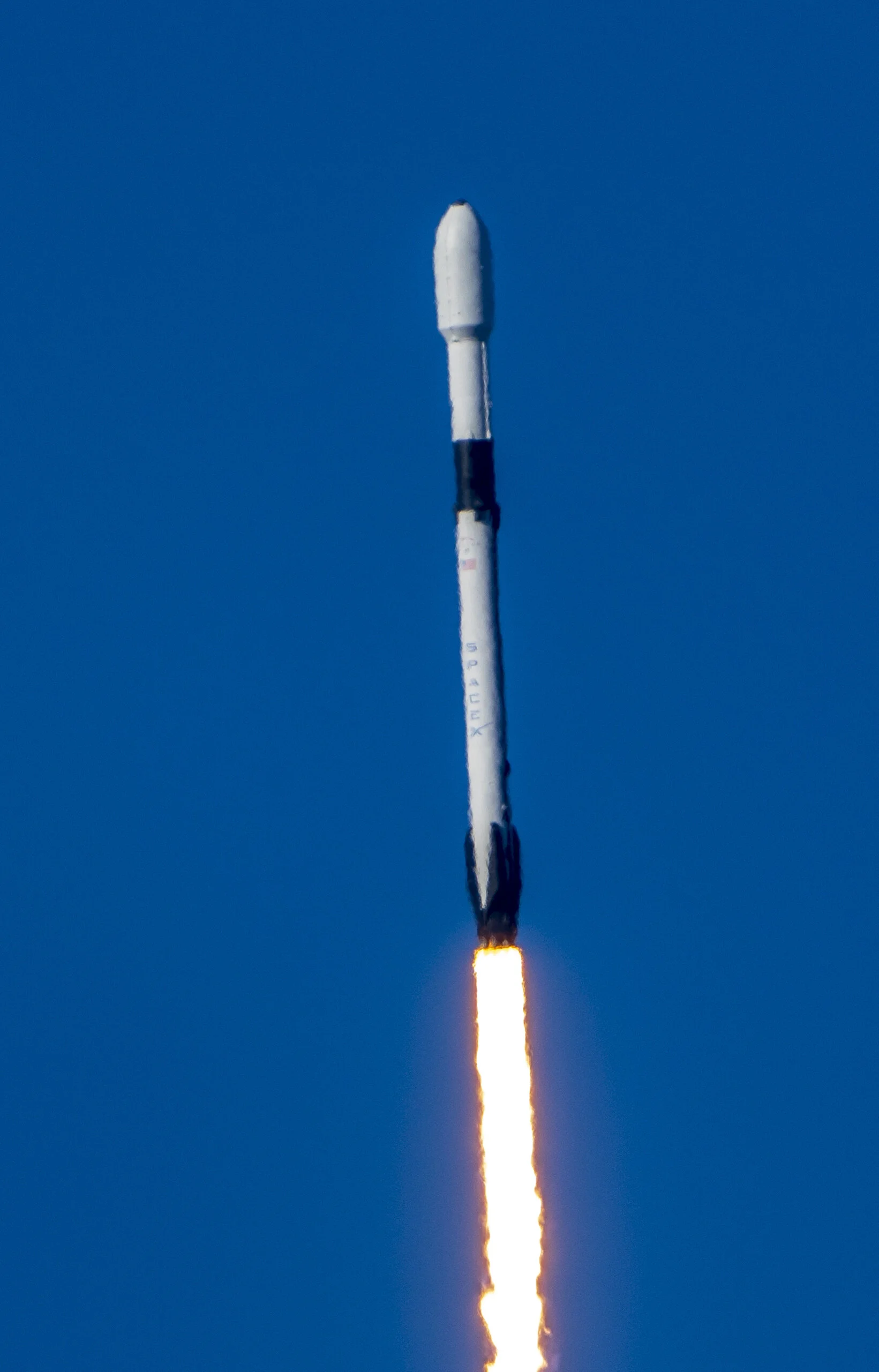 A rocket launching into the sky with flames and smoke coming from its engines against a clear blue sky.