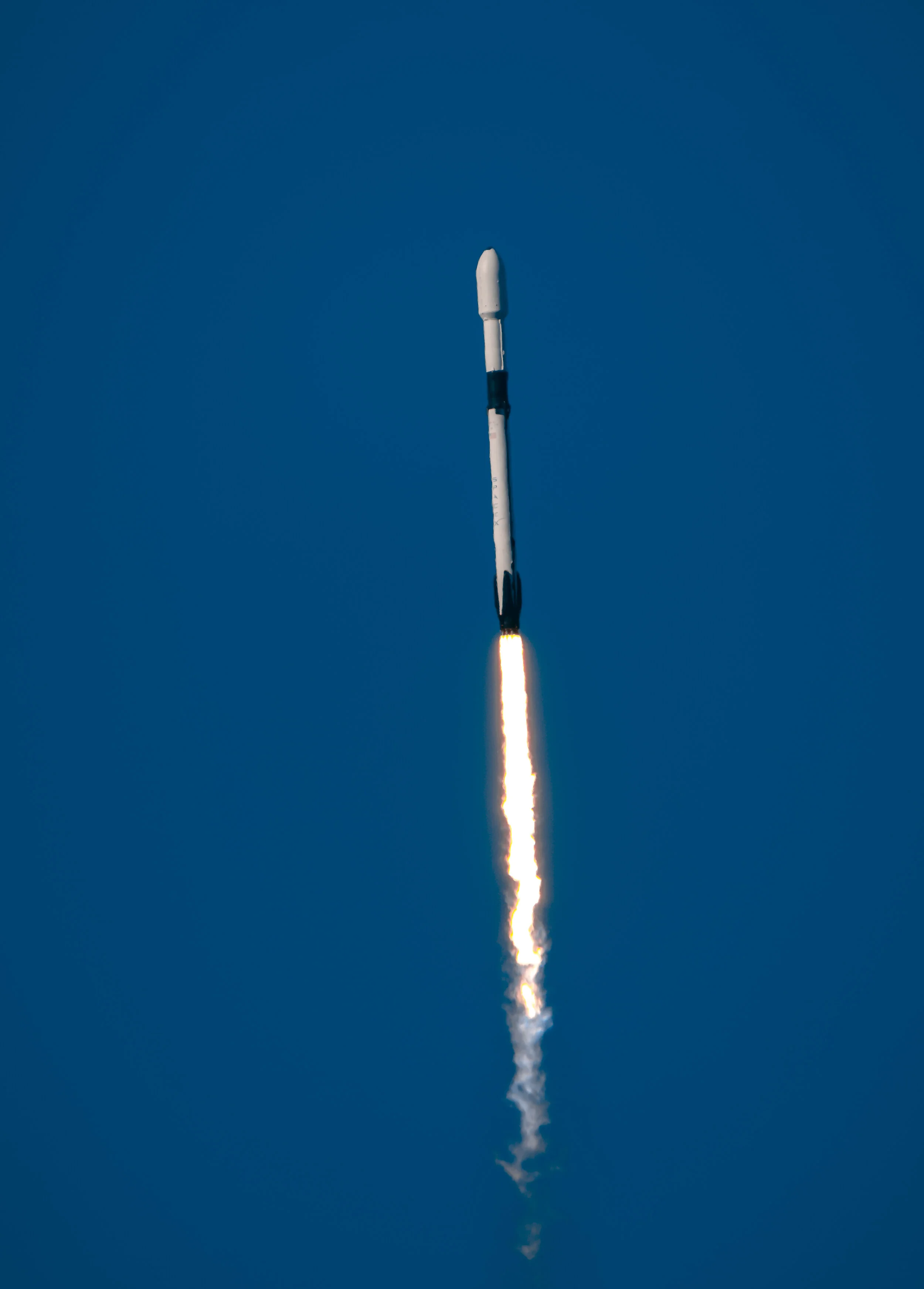A rocket launching into the sky with a trail of flames and smoke beneath it against a clear blue sky.