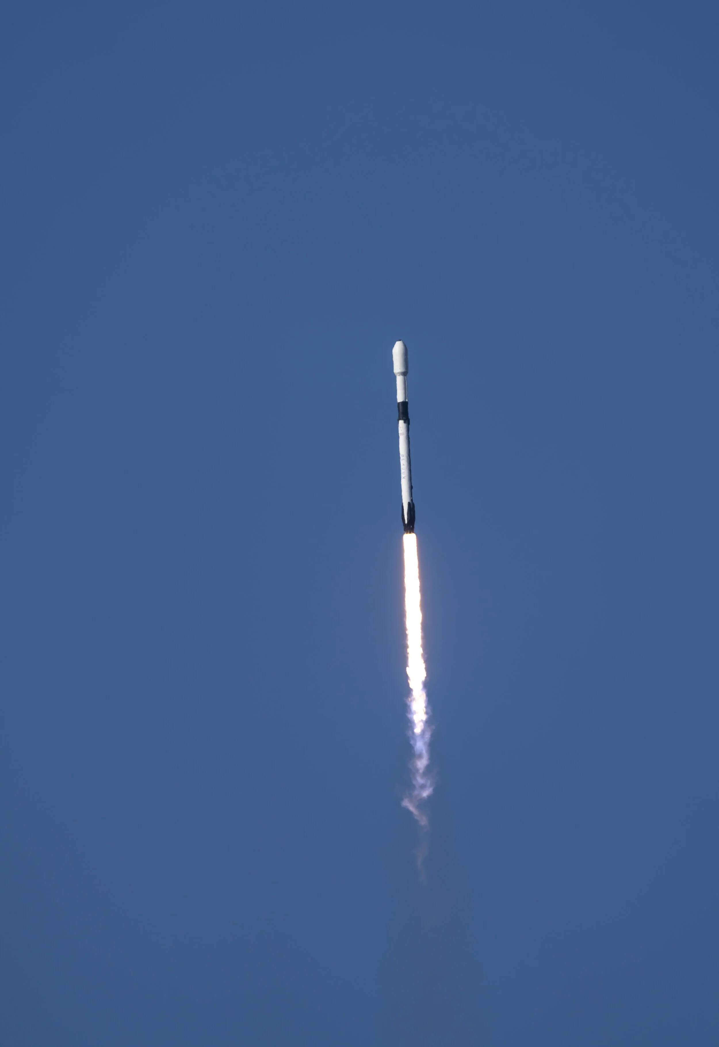 Rocket launch with the rocket ascending into a clear blue sky and a trail of smoke and fire below.