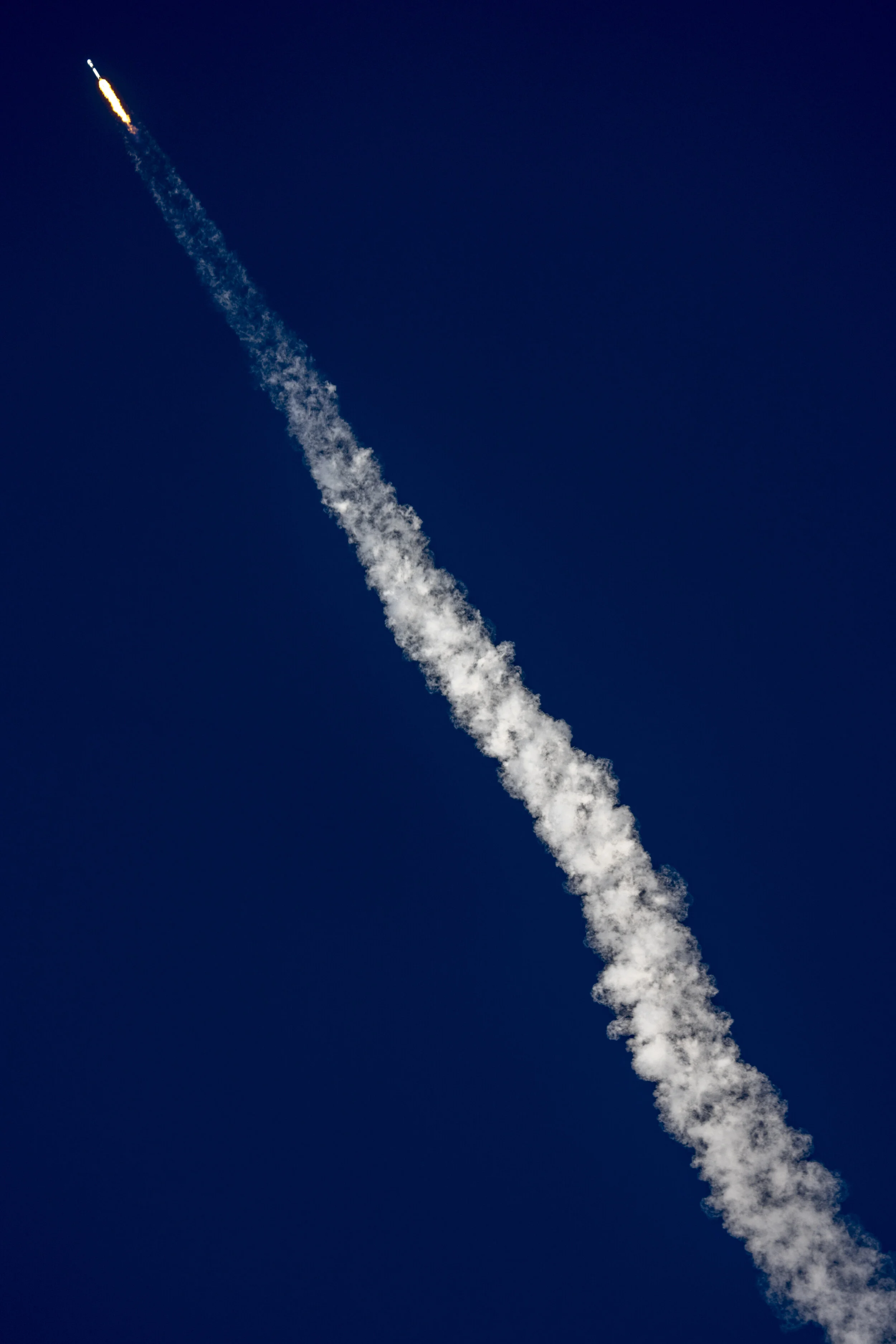 A rocket launching into a clear blue sky, leaving a white smoke trail behind.