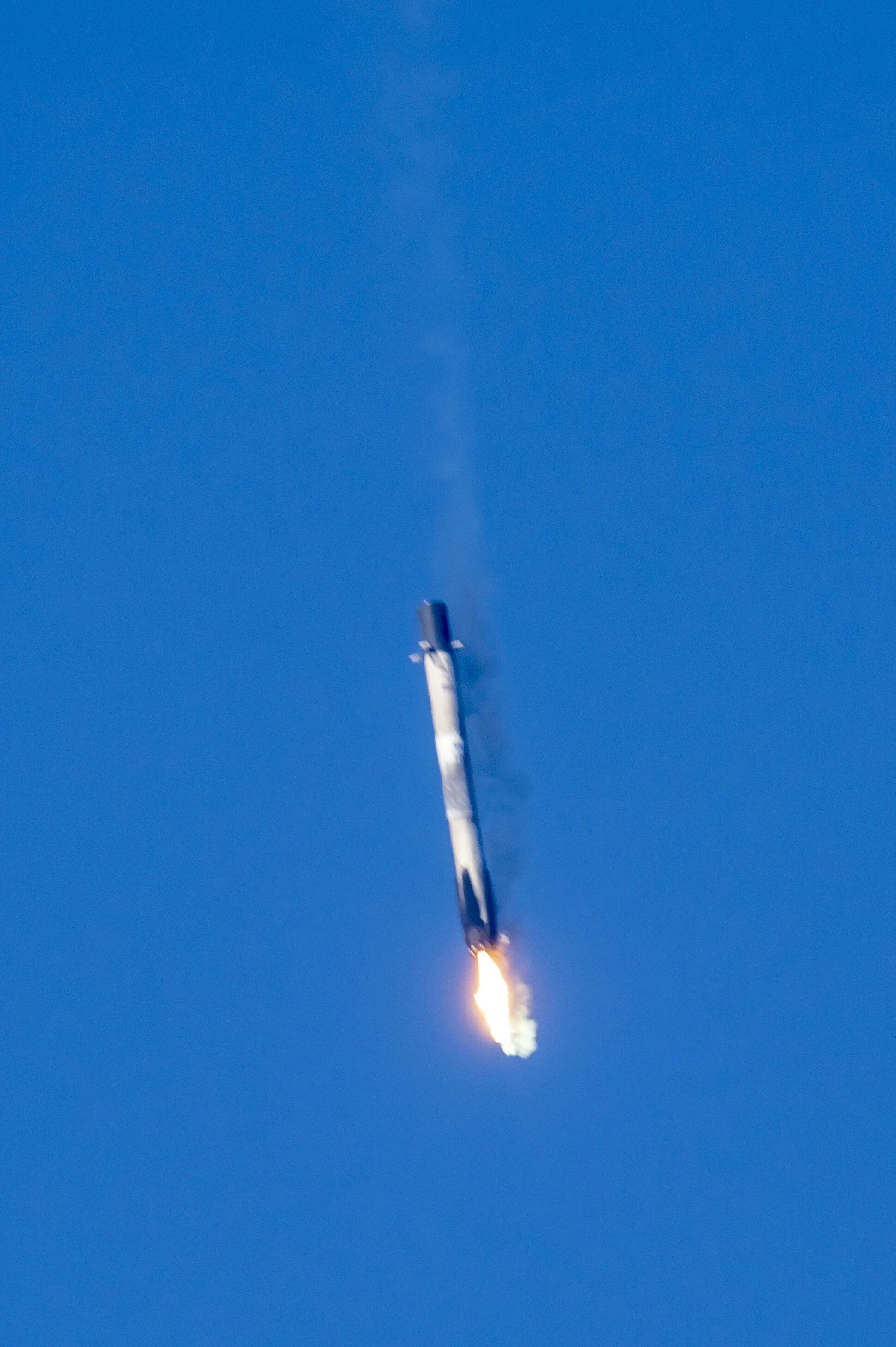 A rocket launching into the sky with a trail of fire and smoke against a clear blue sky.