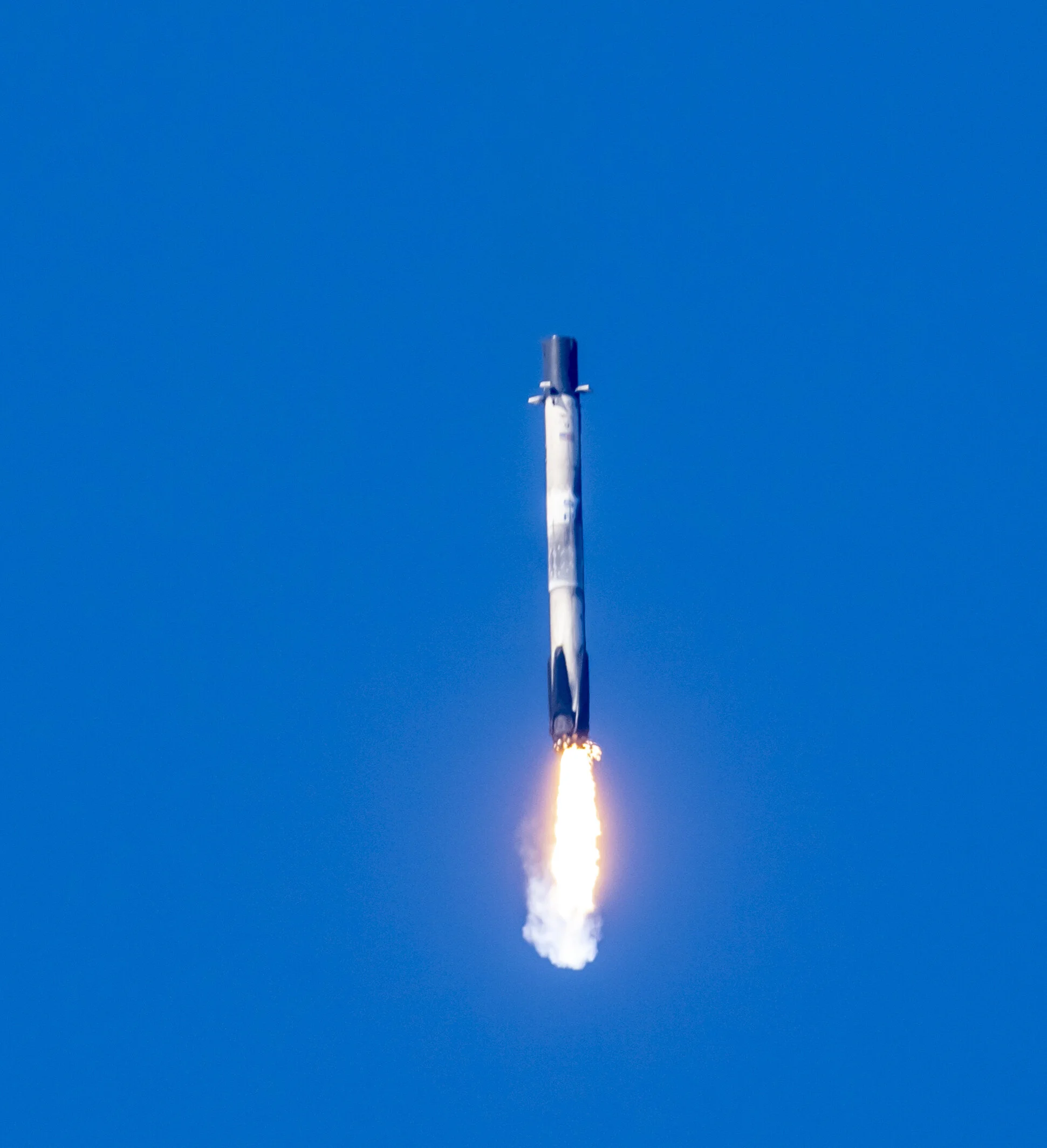 A rocket launching into the clear blue sky with a trail of fire and smoke beneath it.