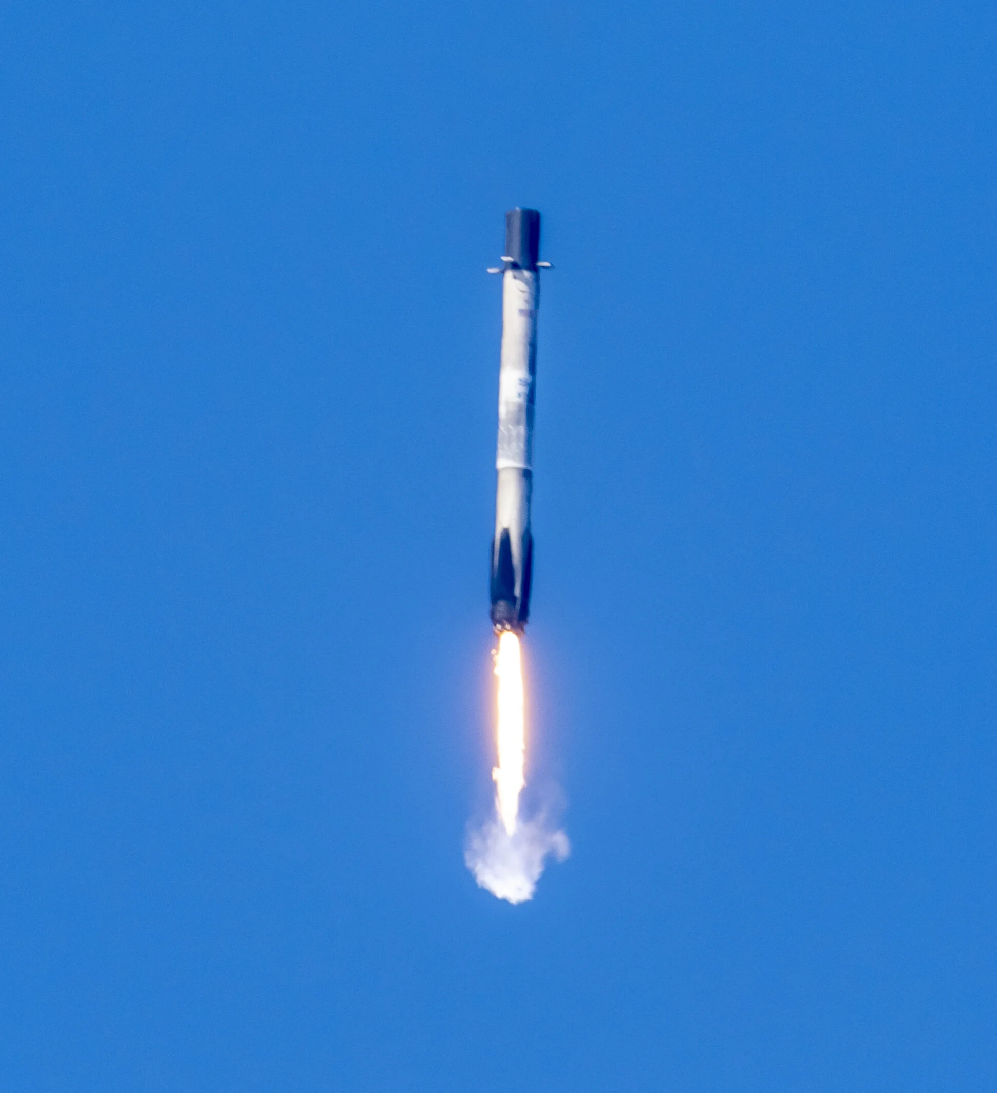 A rocket launching into a clear blue sky with visible flames and smoke at the bottom.