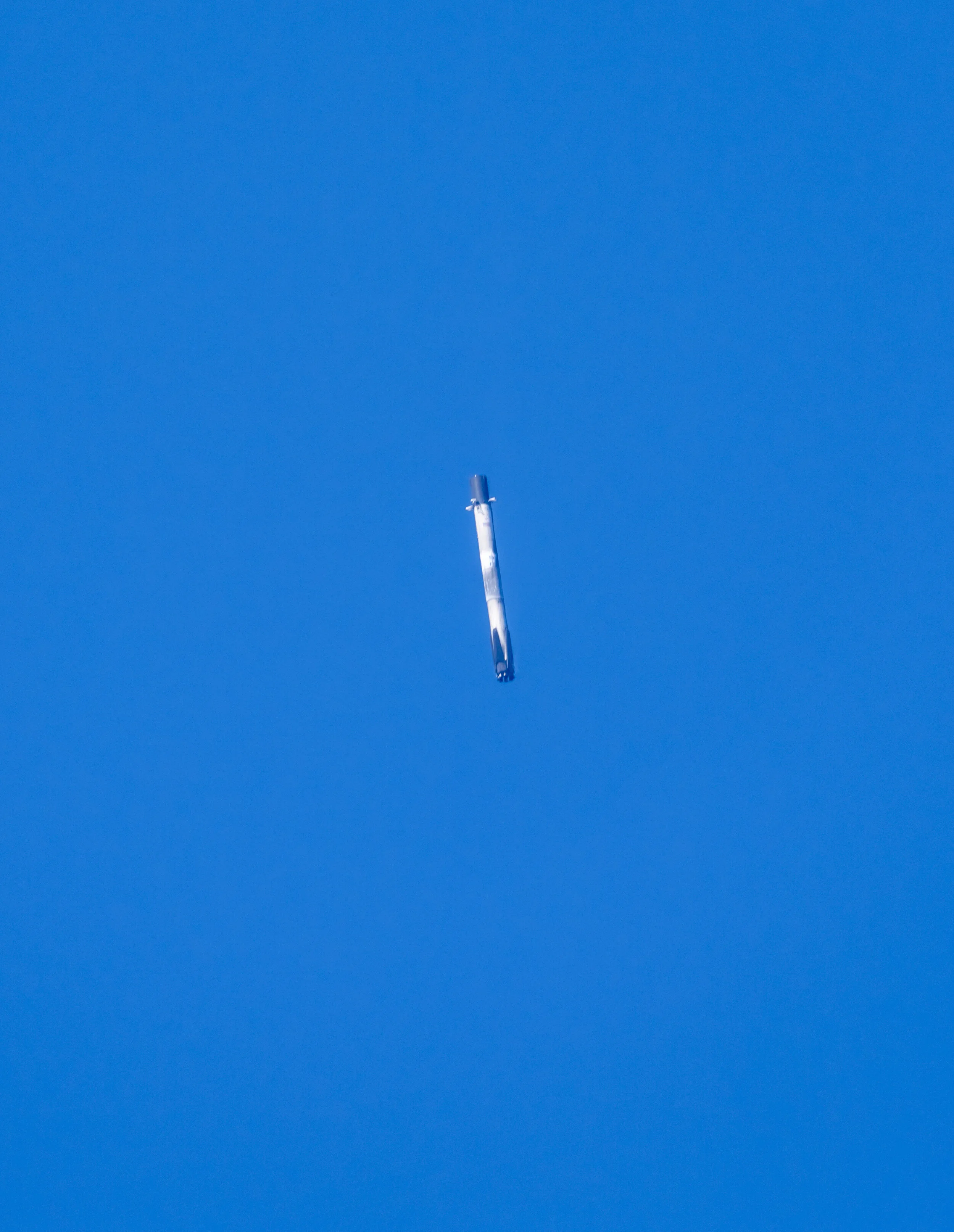 A rocket ascending into a clear blue sky, with only a small white and gray portion of the rocket visible at the bottom of the image.