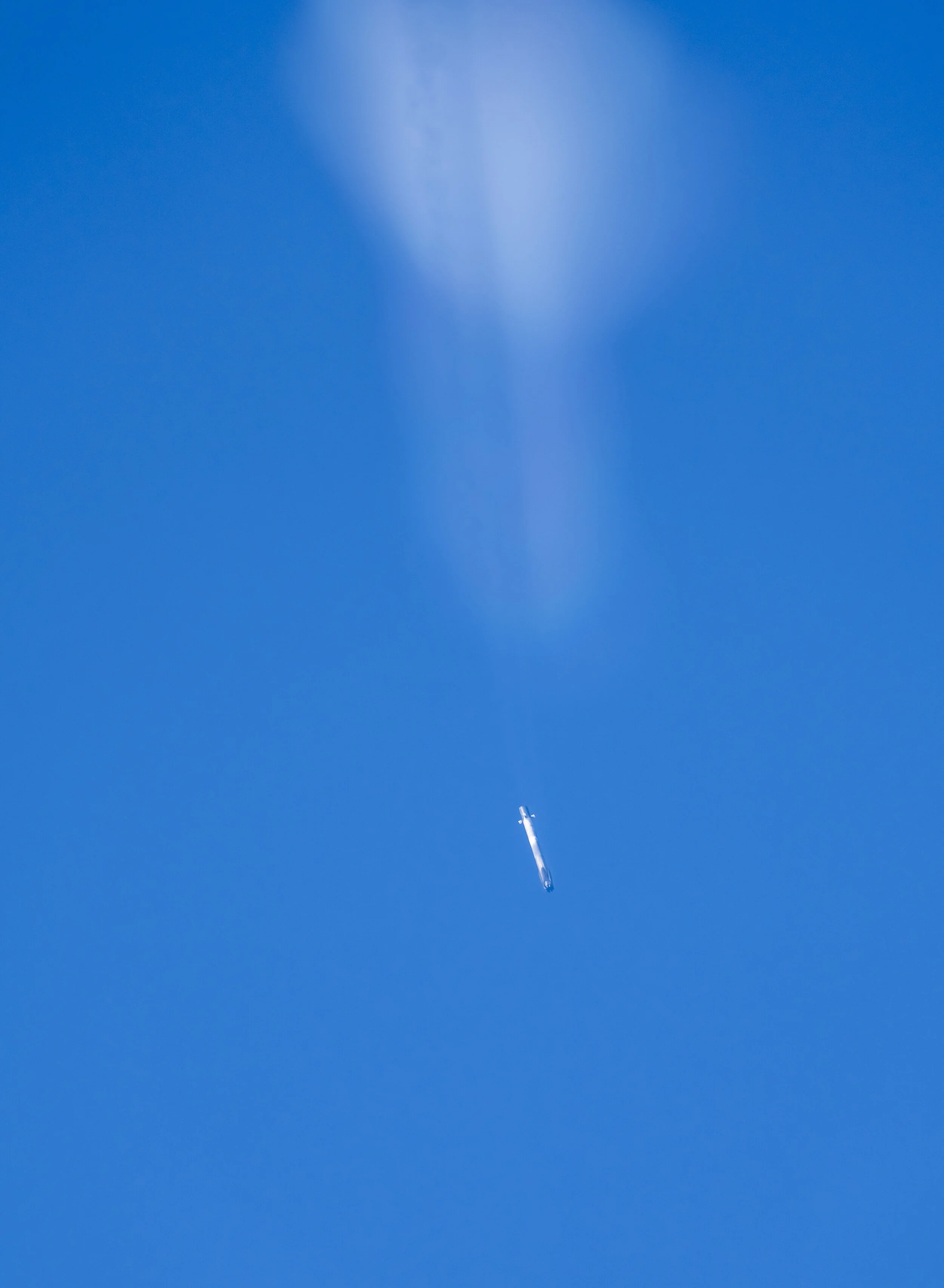 A clear blue sky with a small aircraft flying at the bottom, trailing a thin line of white vapor or condensation.