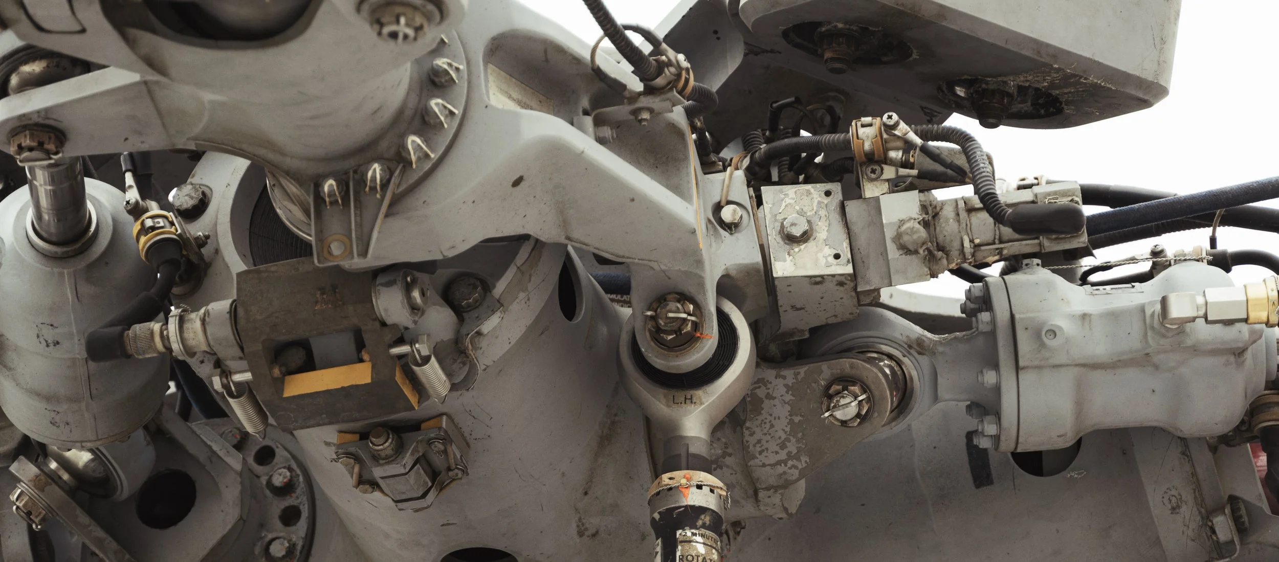 Close-up of mechanical components of an aircraft, including metal parts, hydraulic tubes, and connectors, showing signs of wear and dirt.