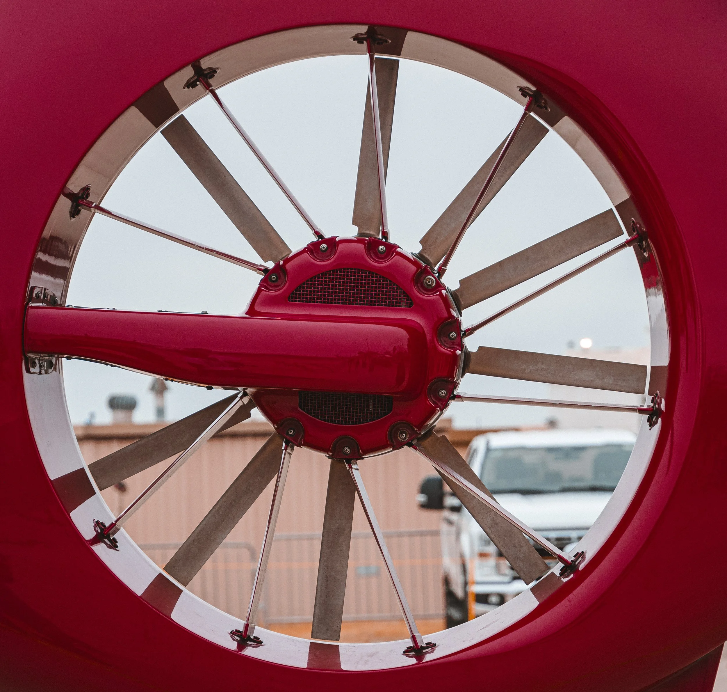 Looking up into the inside of a red baseball or softball foul pole with a sky and distant buildings in the background.