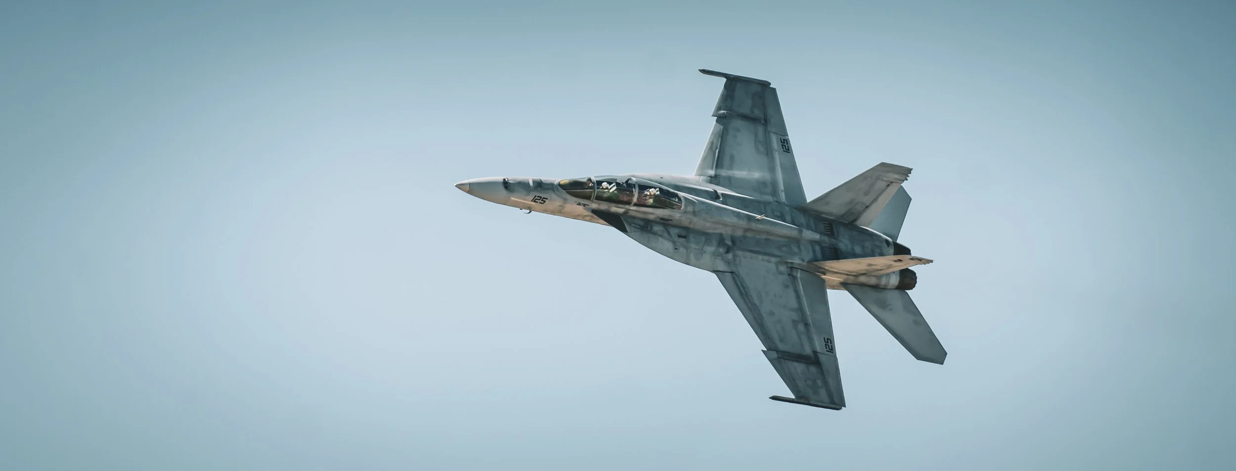 A military fighter jet flying in clear blue skies.