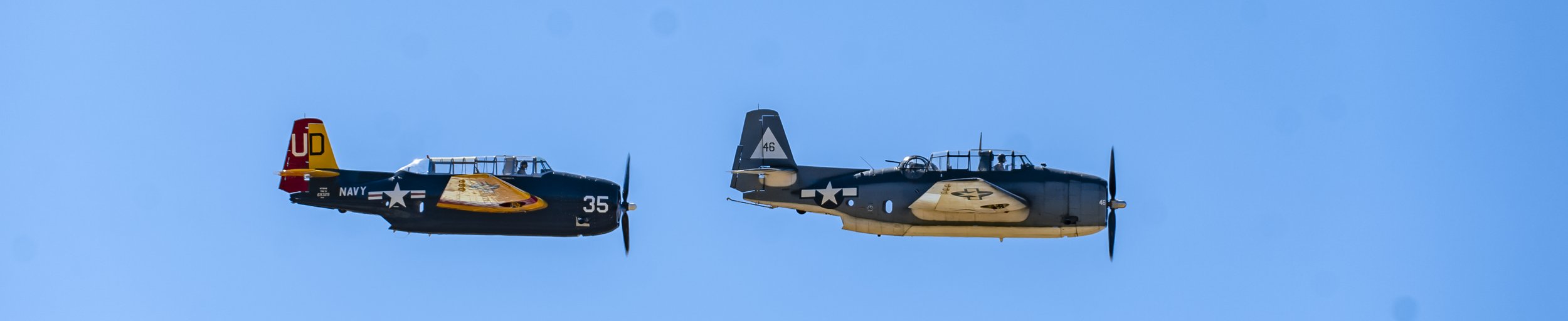 Two vintage military propeller planes flying in the sky side by side.