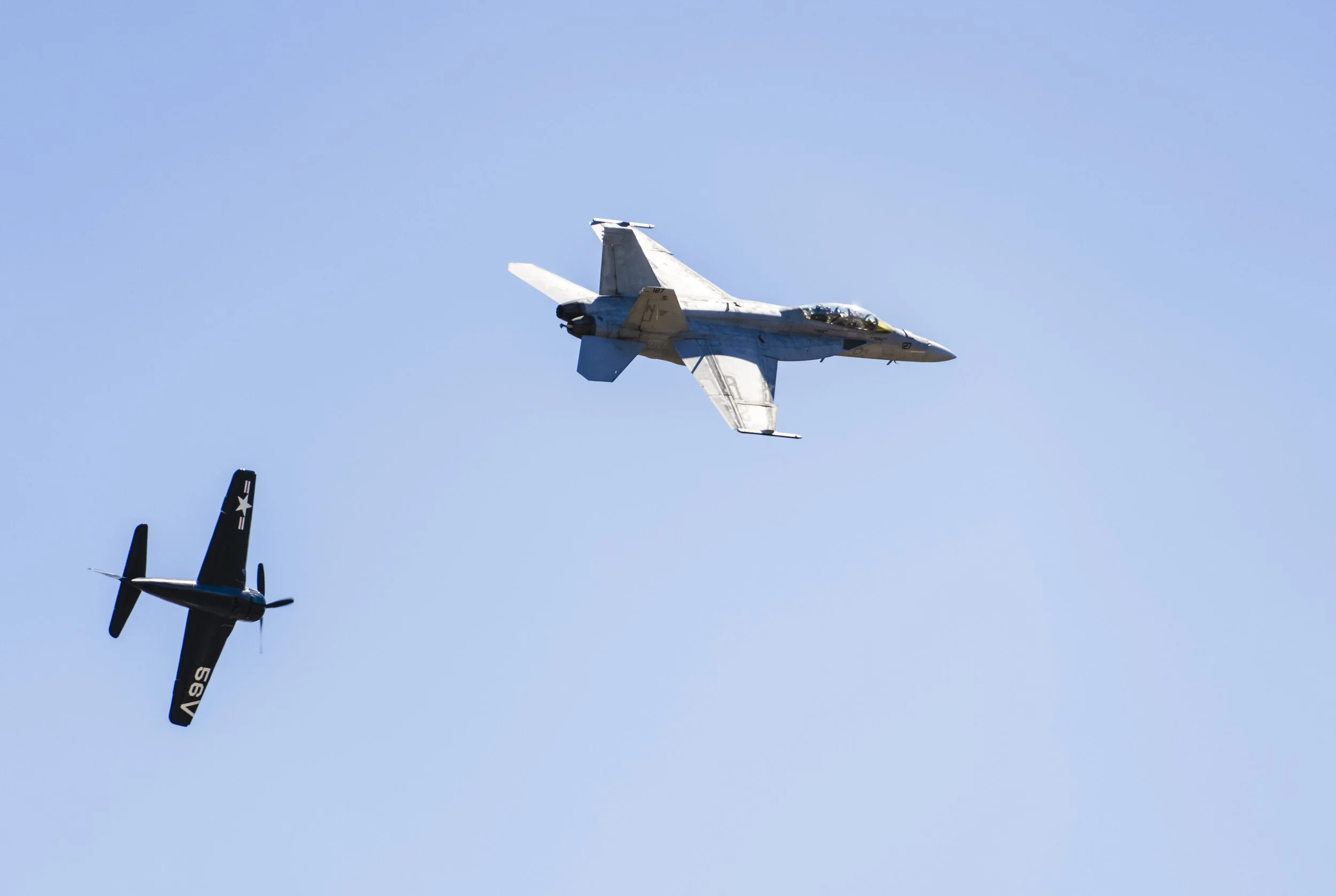 Two fighter jets flying in formation against a clear blue sky, with one jet upside down.