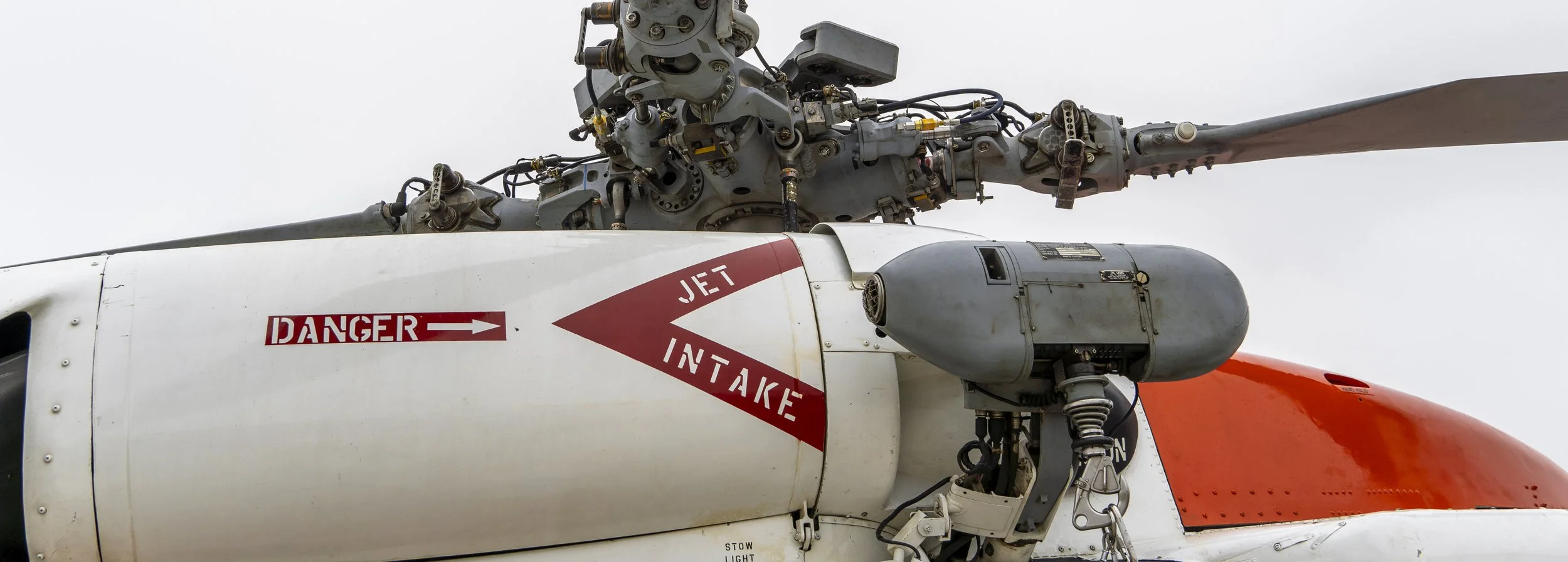Close-up of a helicopter's rotor and nose section, with a danger warning label indicating 'Jet Intake' and an overcast sky in the background.