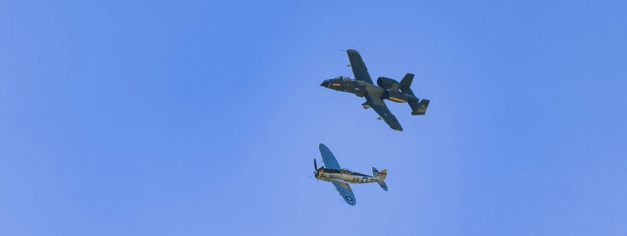 Two vintage fighter aircrafts flying in formation against a clear blue sky.