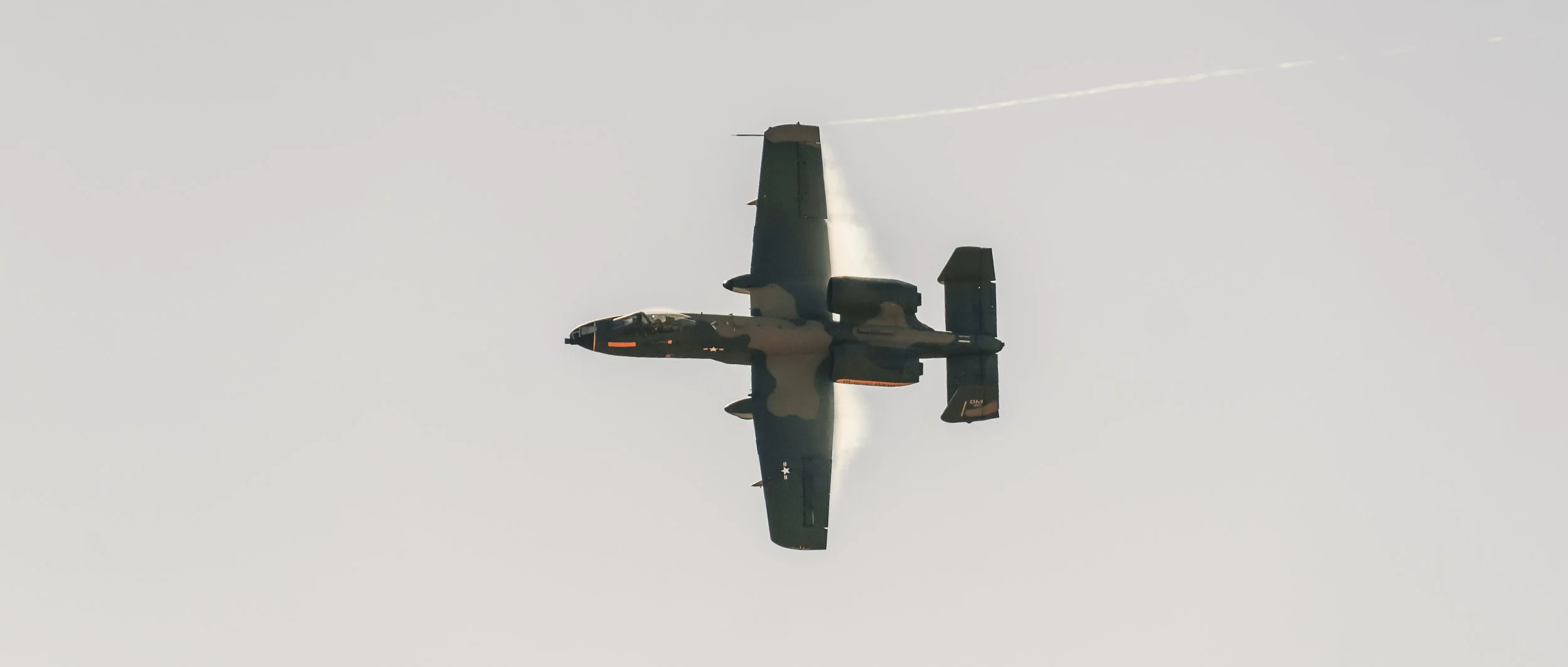 A military fighter jet flying in the sky, leaving a faint vapor trail behind.