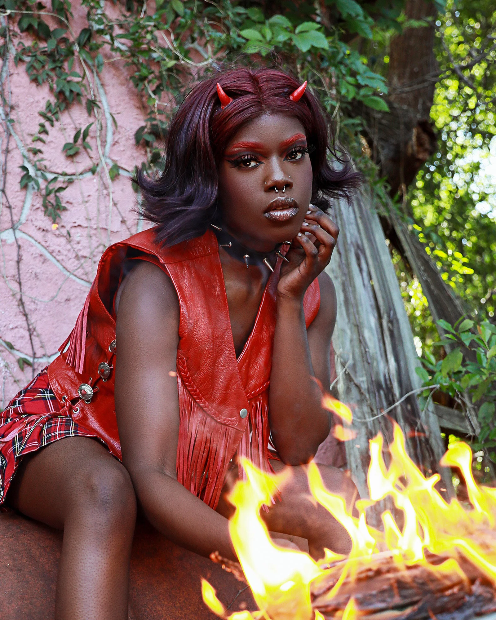 "She Devil" character portrait in red leather and horns, burning papers on a rusted barrel, gothic punk styling — KEN X KEEN Orlando