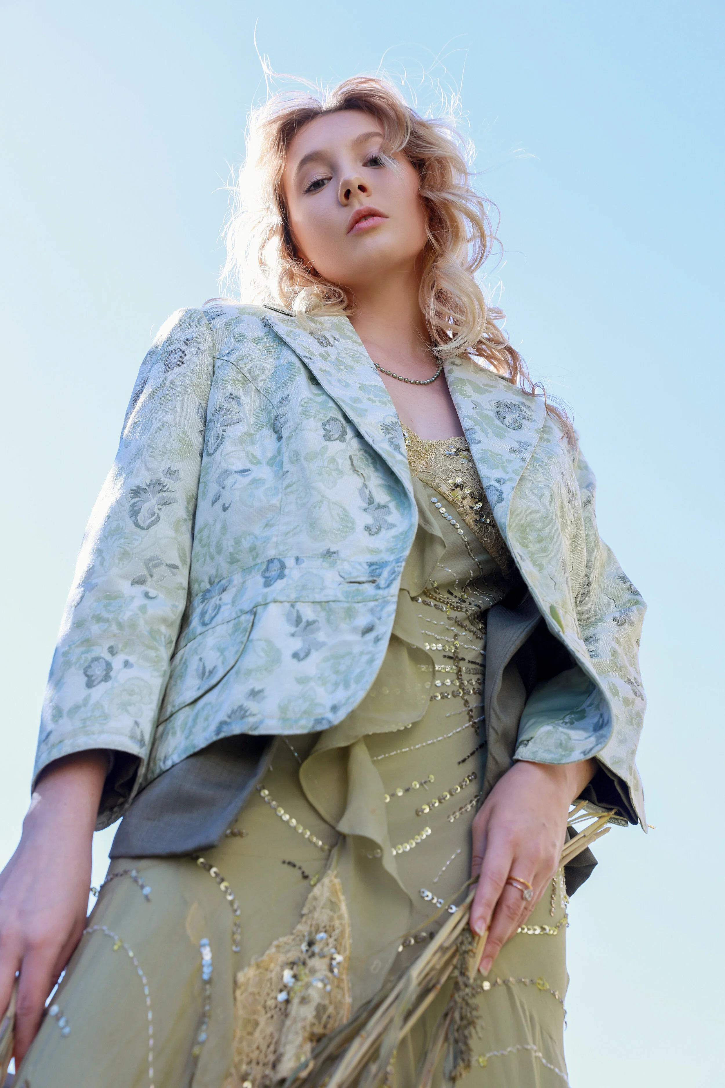 Model in green editorial styling against a clear sky, gazing downward as if swaying in the wind — KEN X KEEN Orlando