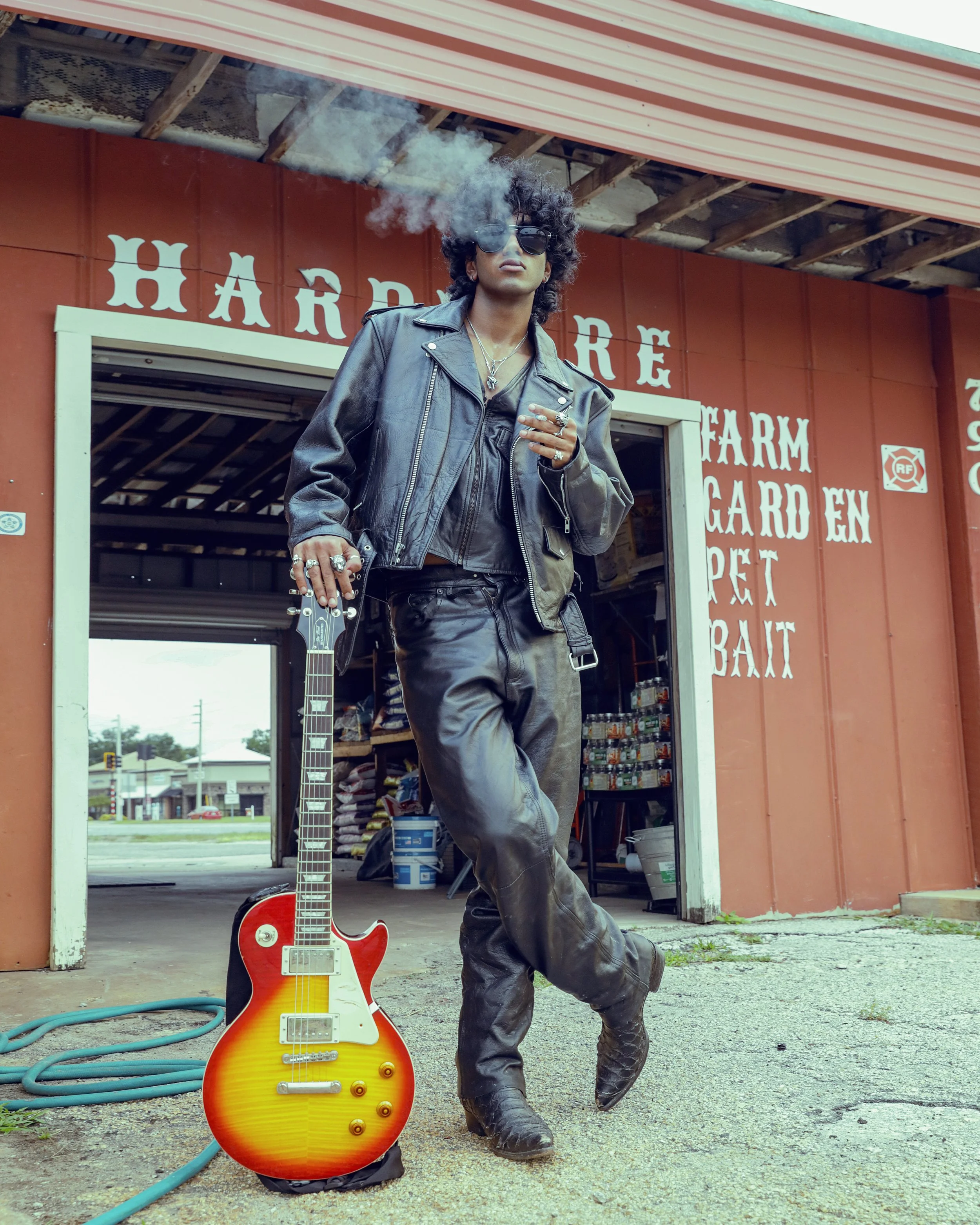 Model in all black leather with a guitar and lit cigarette, biker-inspired portrait outside a vintage hardware store — KEN X KEEN Orlando