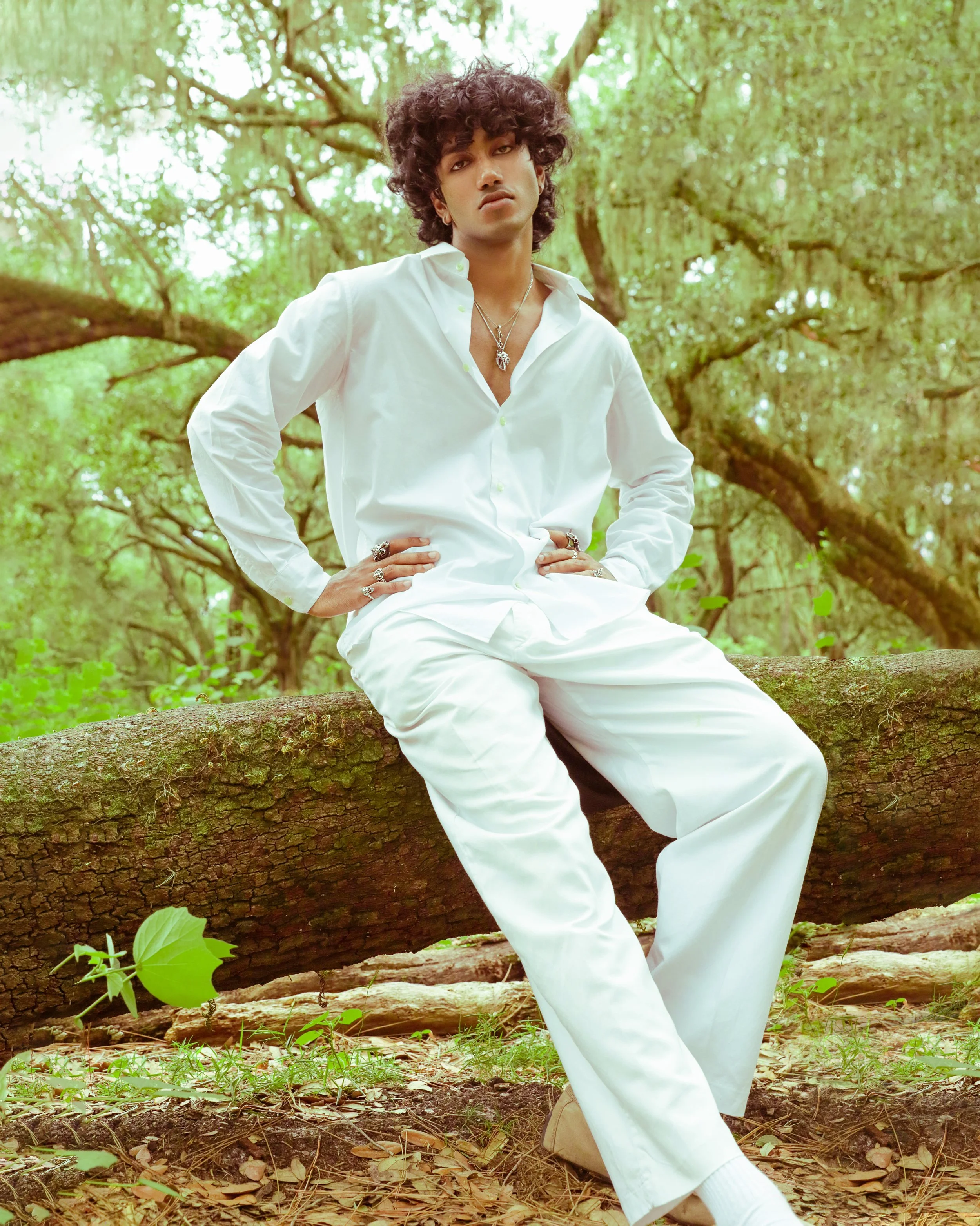 Model in all-white styling leaning against a tree in a lush green forest — natural editorial portrait, KEN X KEEN Orlando.