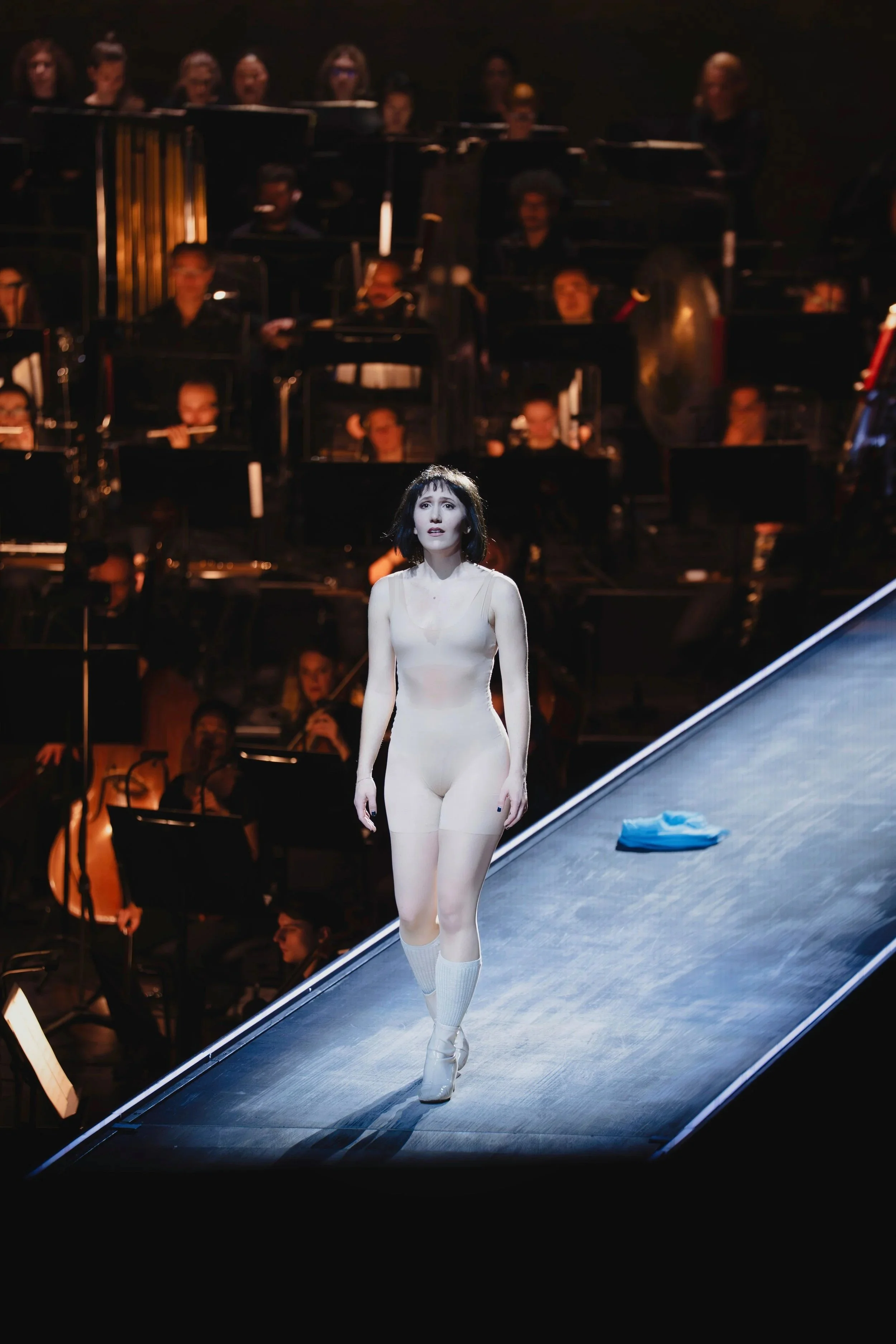 A woman walking on a stage with an orchestra in the background.
