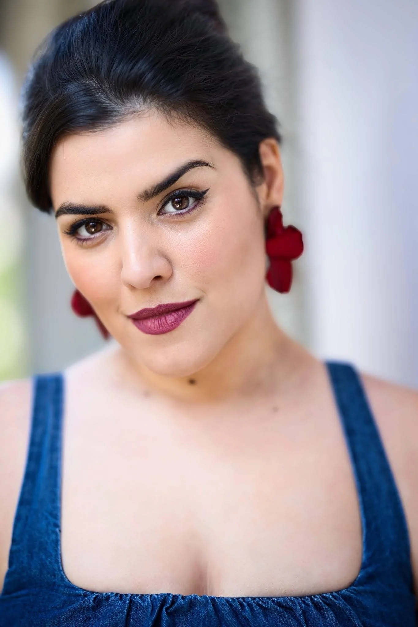 Close-up of a woman with dark hair and brown eyes, wearing red earrings and a blue top.