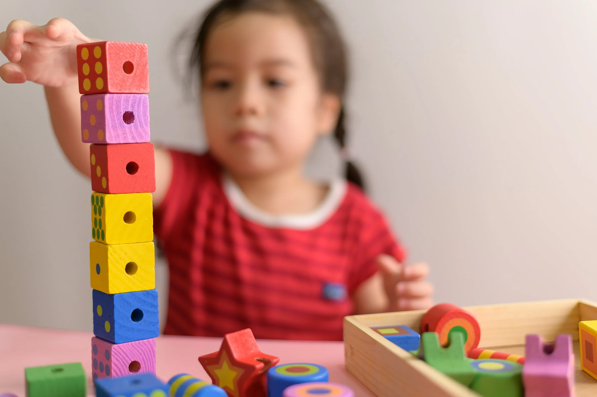 Little curly asian girl enjoy playing with wooden toy blocks iso