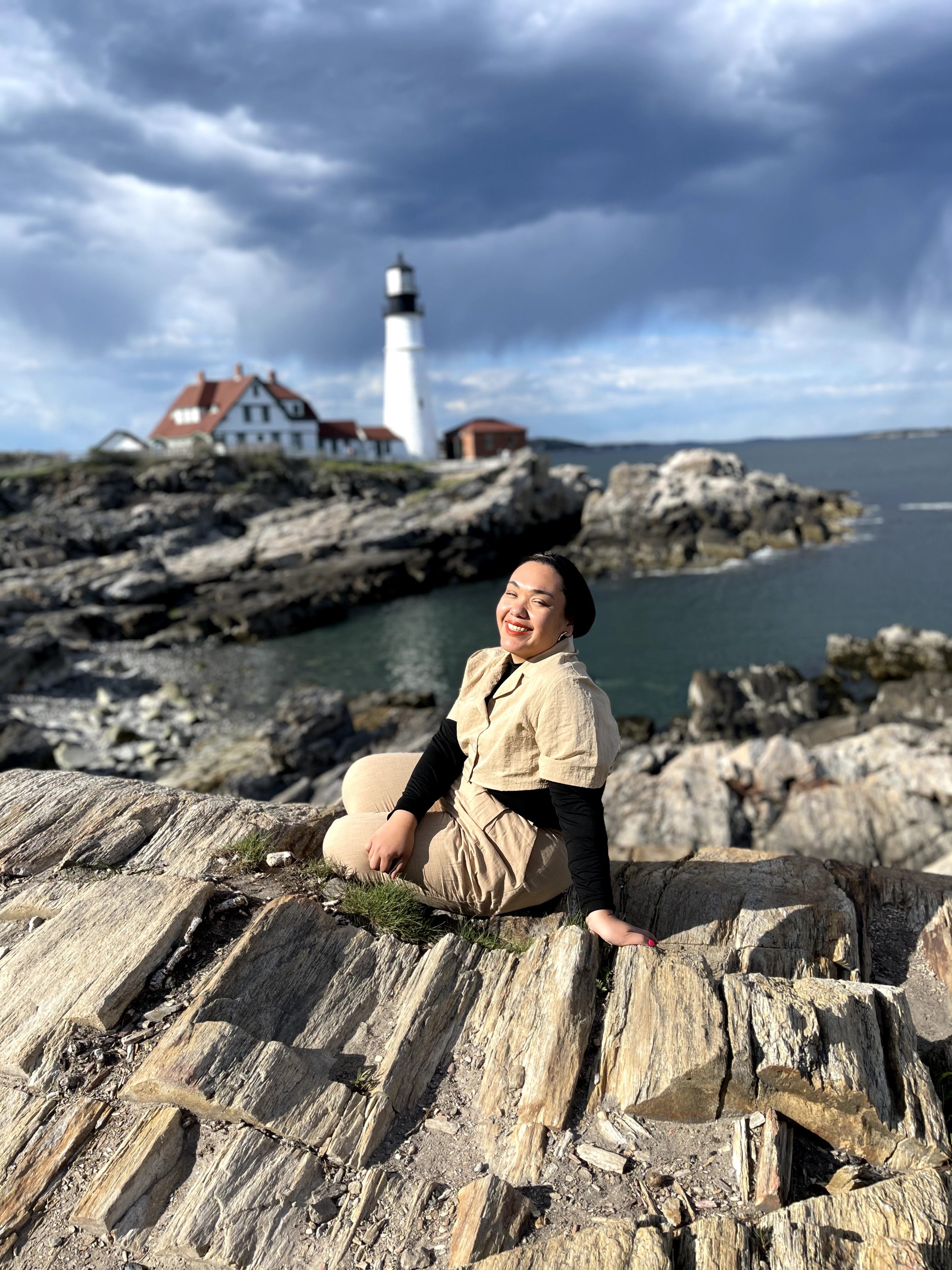 woman with head covering in front of water and light house in portland maine
