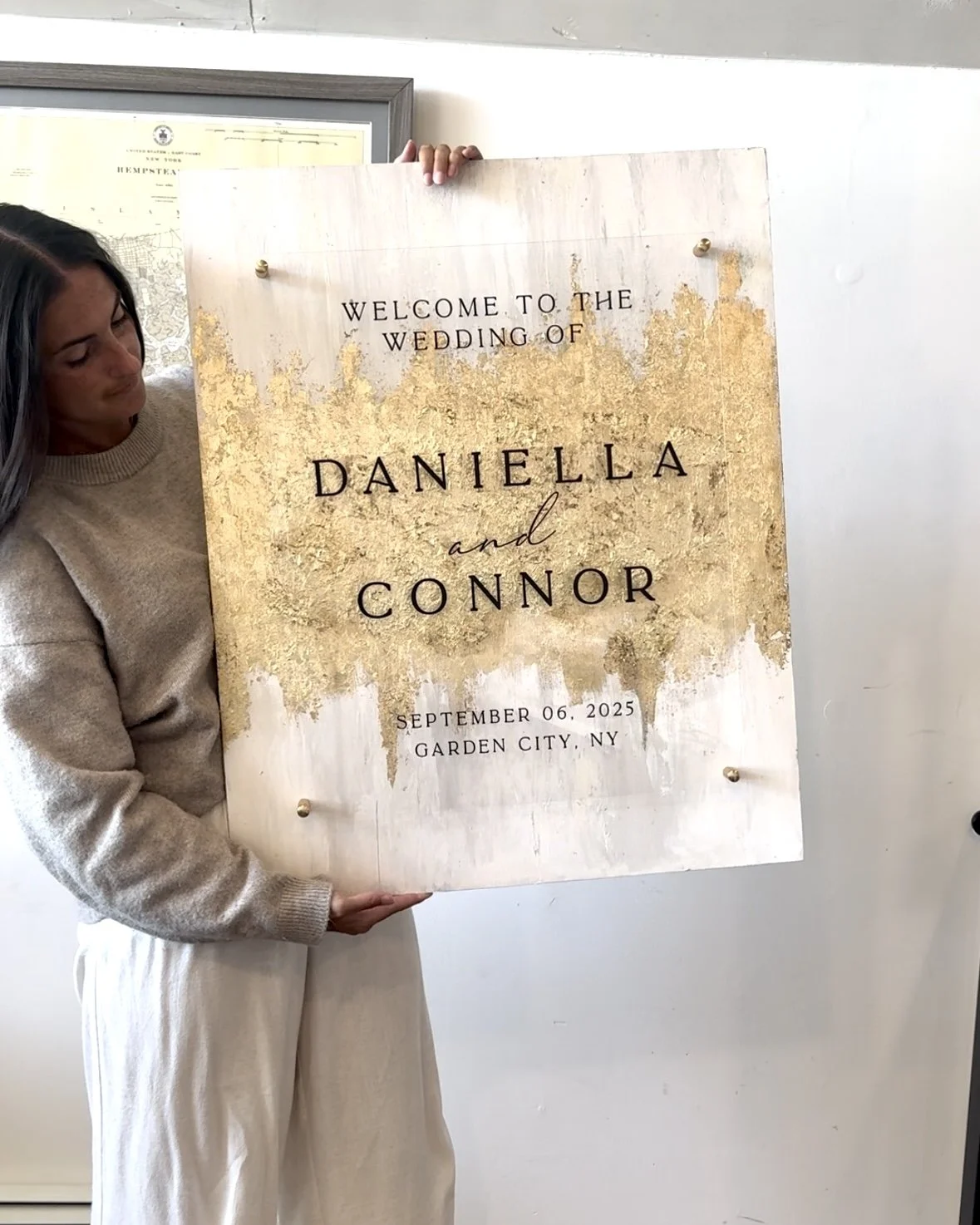 Woman holding a wedding sign with gold and white design for Daniela and Connor's wedding on September 6, 2025, in Garden City, NY.
