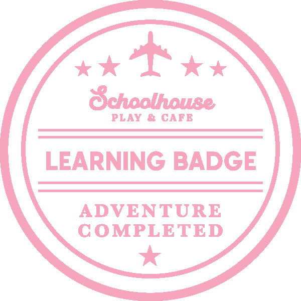 Pink and white circular badge with airplane icon and stars, reading "Schoolhouse Play & Cafe," "Learning Badge," and "Adventure Completed."