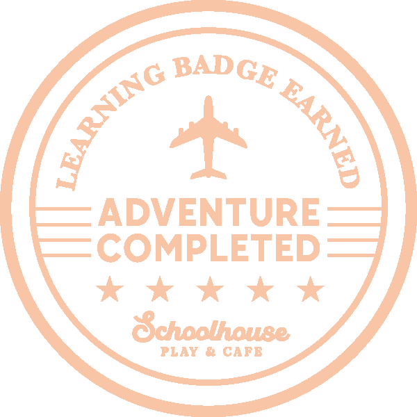 A circular badge with the text 'Learning Badge Earned' at the top, an airplane icon in the center, and 'Adventure Completed' below it. The badge also has five stars and the words 'Schoolhouse Play & Cafe' at the bottom.