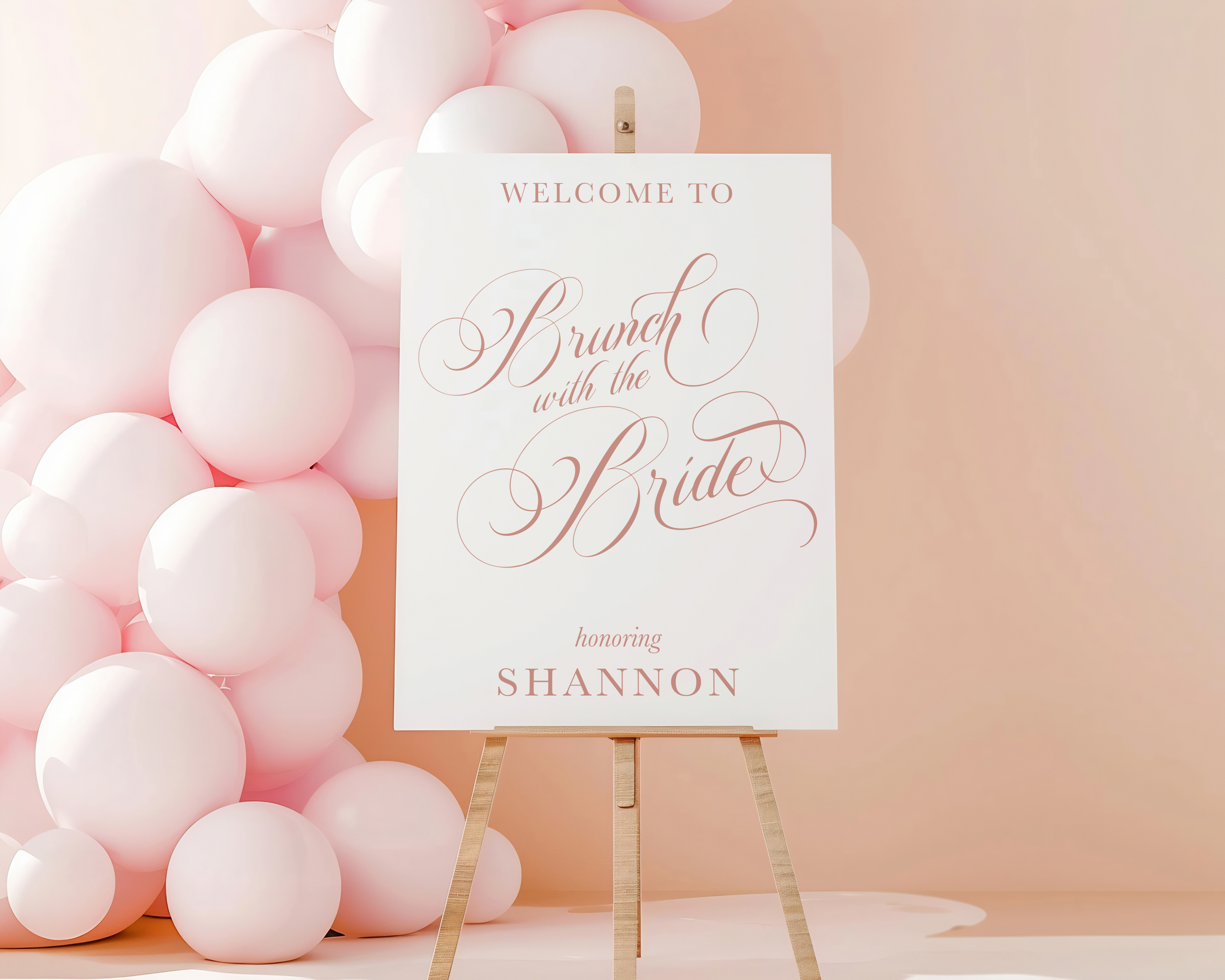 Wedding welcome sign on an easel with pink and white balloons in the background, reading "Welcome to Brunch with the Bride, honoring Shannon."