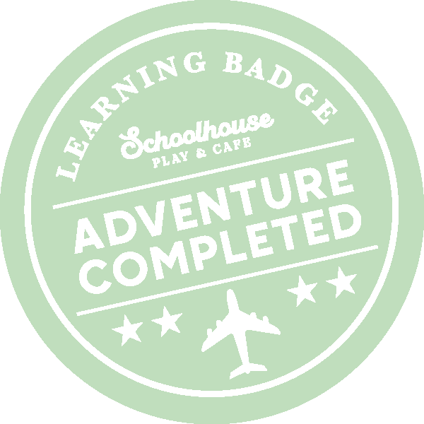 A circular badge with a light green background and white text. It reads "Learning Badge" at the top, "Schoolhouse Play & Cafe" underneath, and "Adventure Completed" prominently in the center. The badge features a small airplane icon at the bottom and three stars.