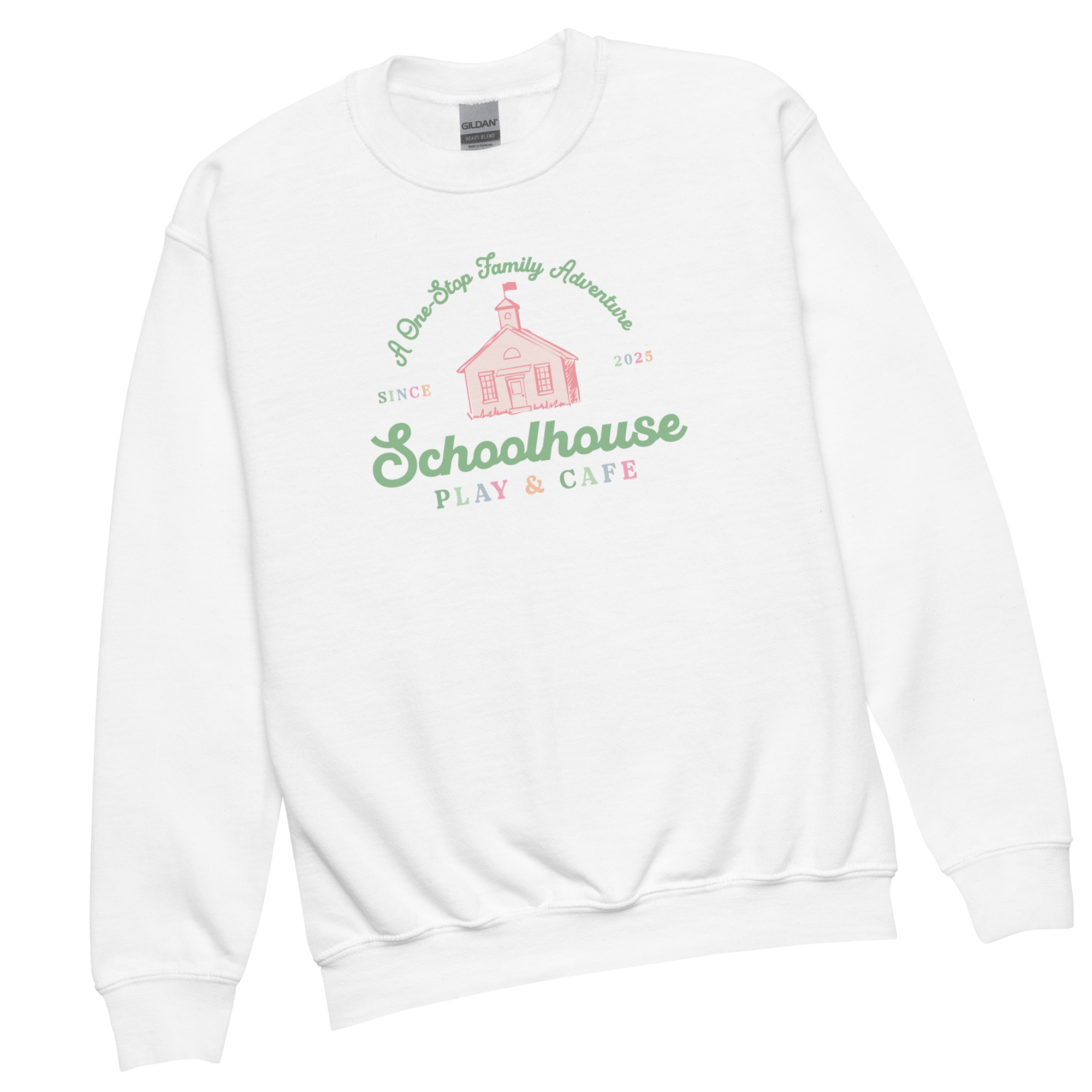 White sweatshirt with a graphic design of a schoolhouse, with text reading "A One-Stop Family Adventure," "Since 2025," and "Schoolhouse Play & Cafe" in green, pink, and orange colors.