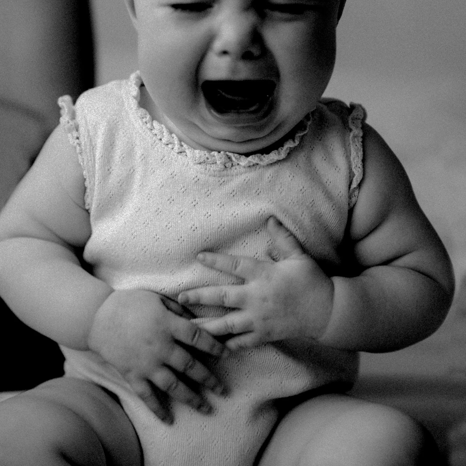 A black and white lifestyle photo of a baby crying and holding their stomach with their little hands