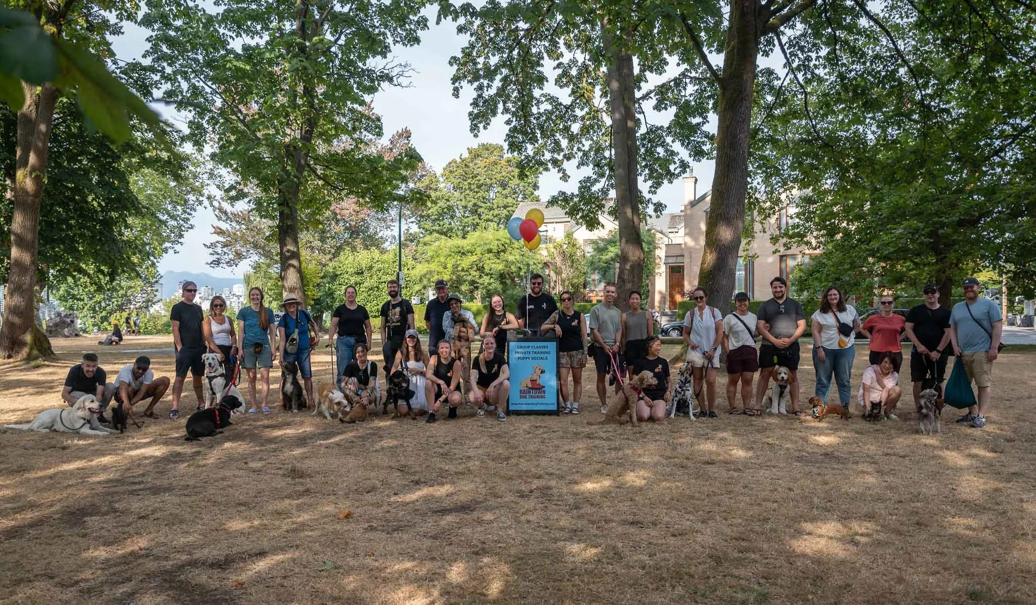 Over twenty dog parents and their dogs surround the Raintown Dog Training team for Raintown's annual summer event.