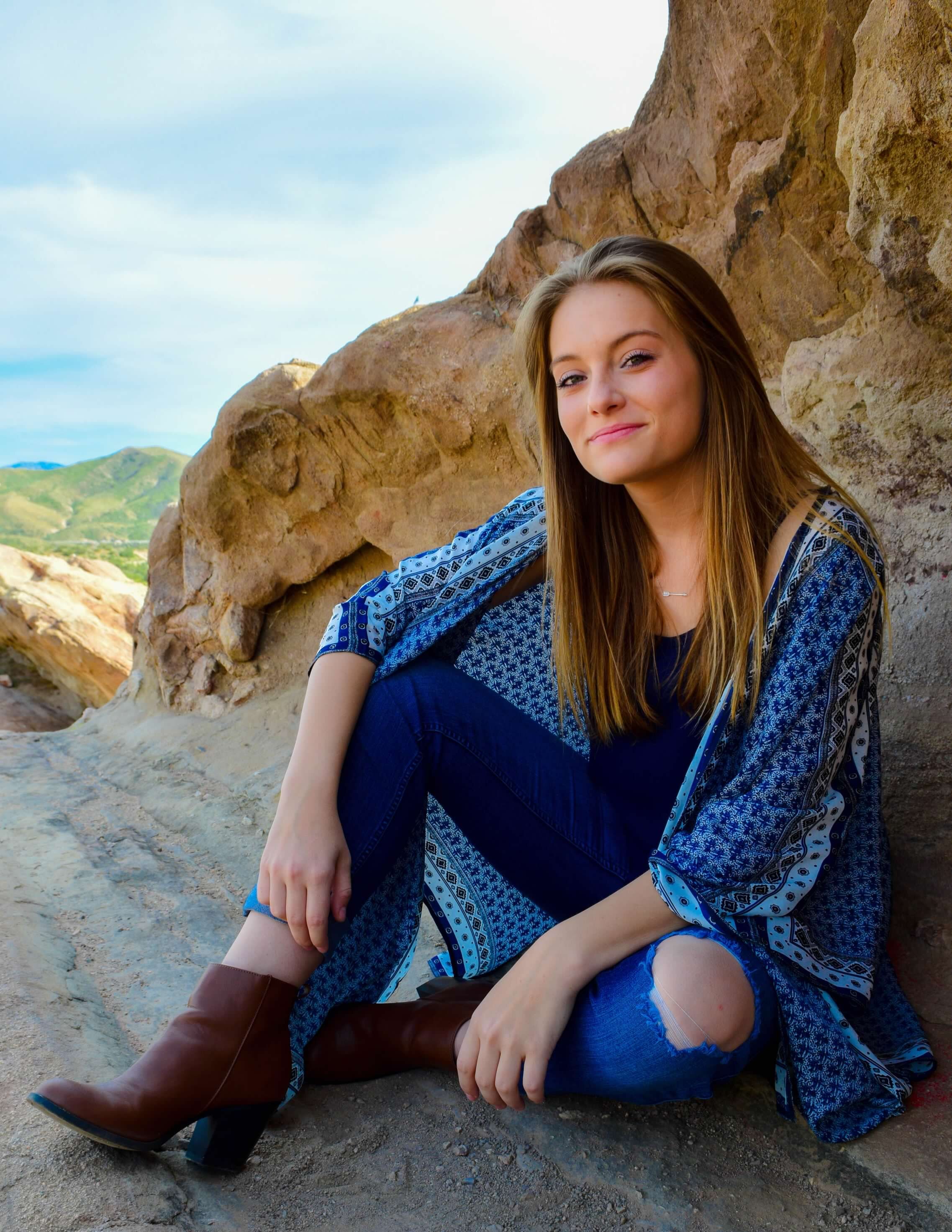 High school girl sitting relaxed on cove of large rock formation, looking happily at camera