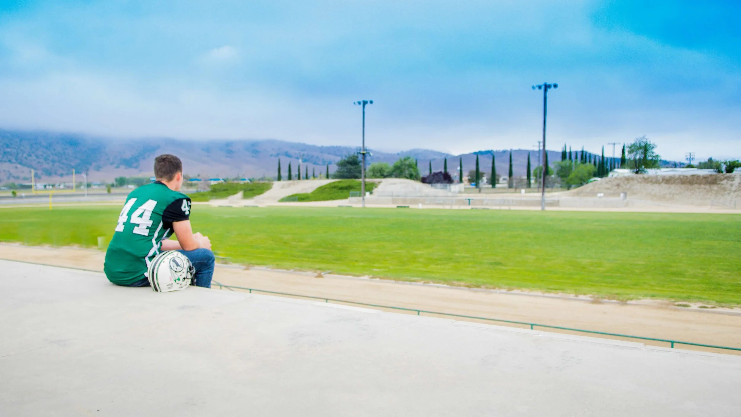 High school senior boy wearing football jersey, facing football field with back toward camera.