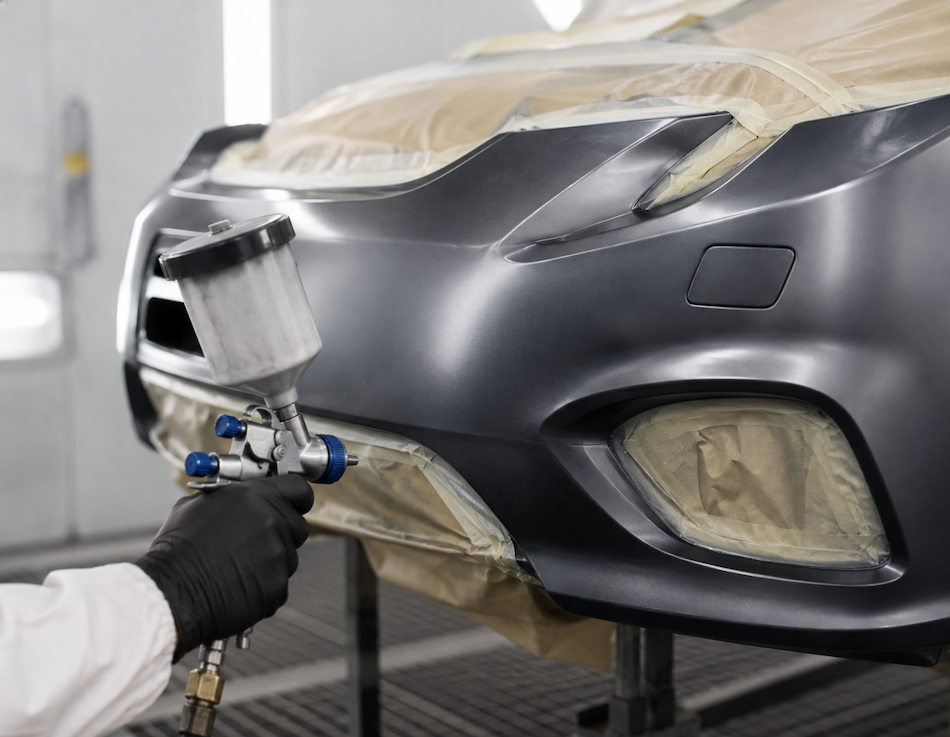 Technician spray painting a car bumper in a professional paint booth