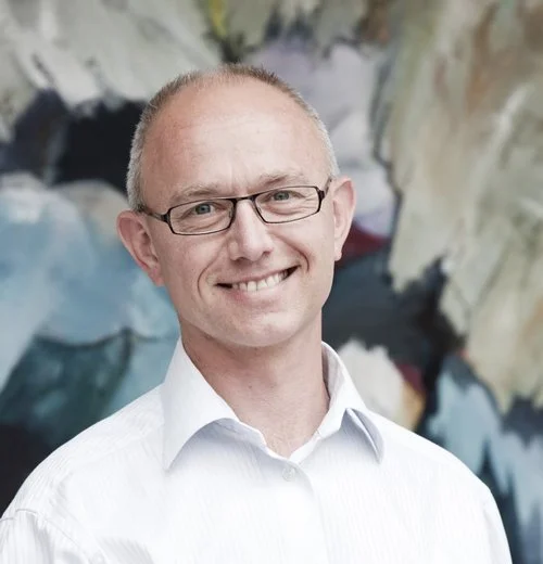 Smiling man wearing glasses and a white shirt with abstract background