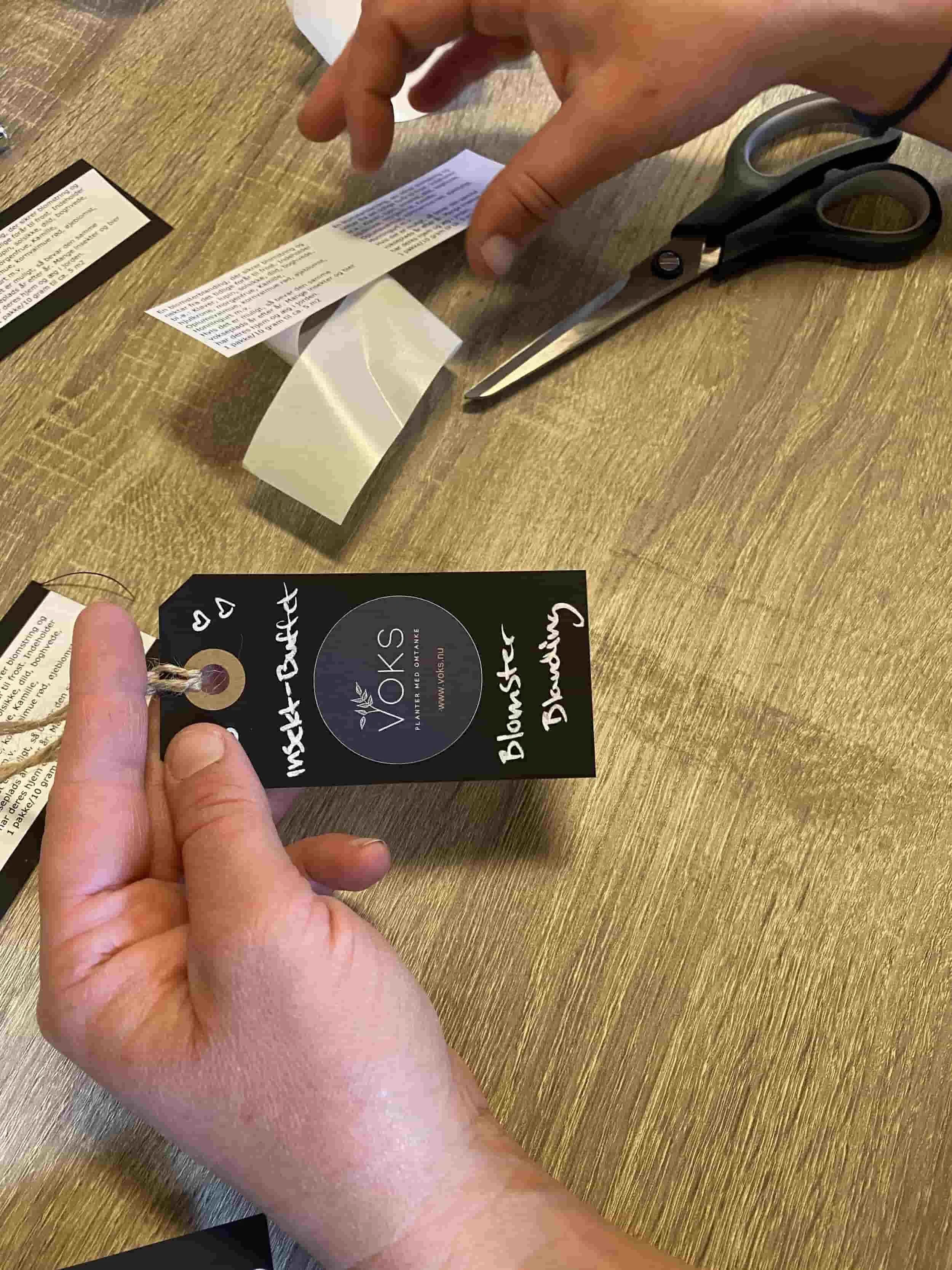 Hånd laver VOKS planteetiket med håndskrevet tekst og logo