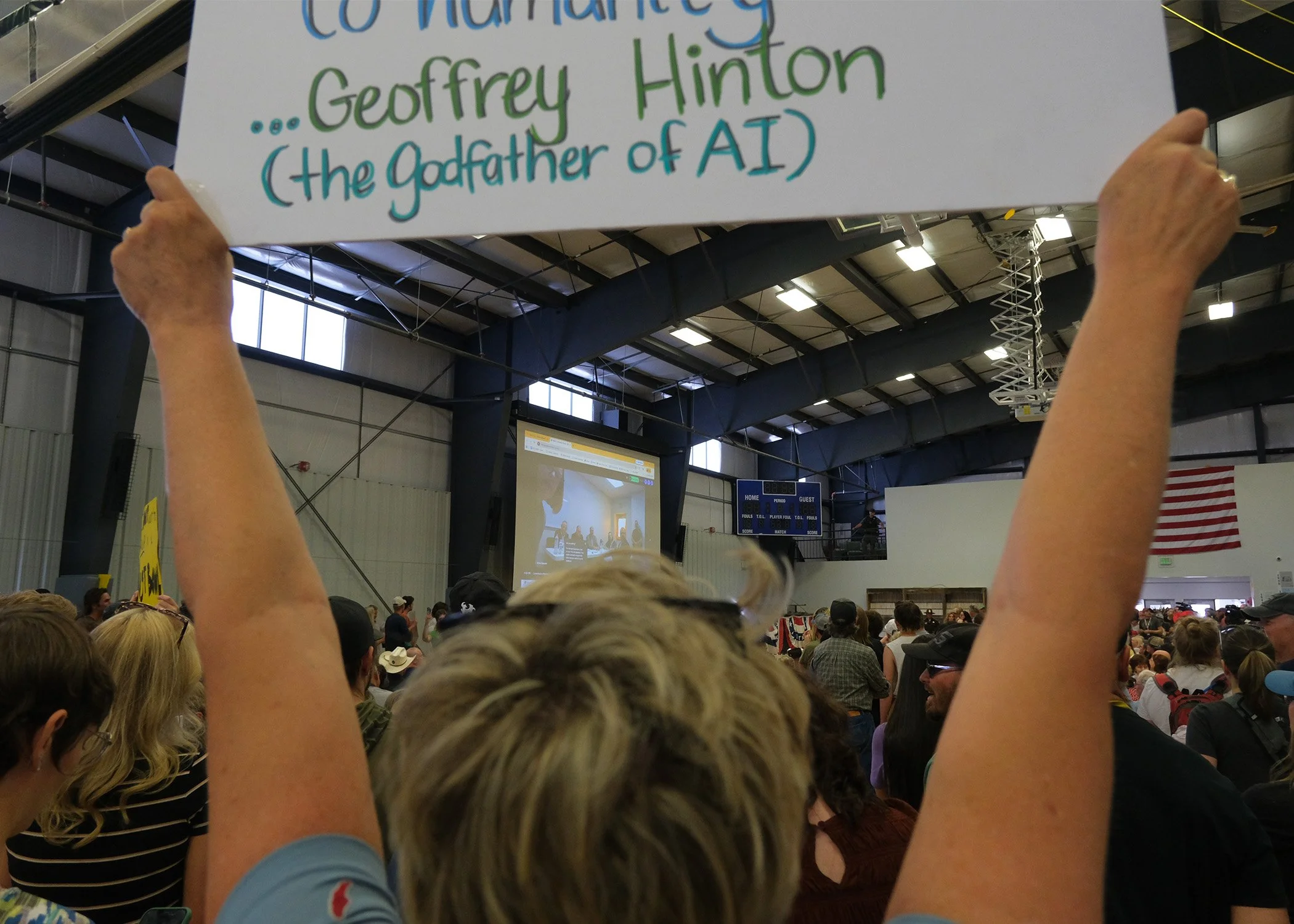 An attendee holds a sign as Box Elder County commissioners prepare a vote via video call.
