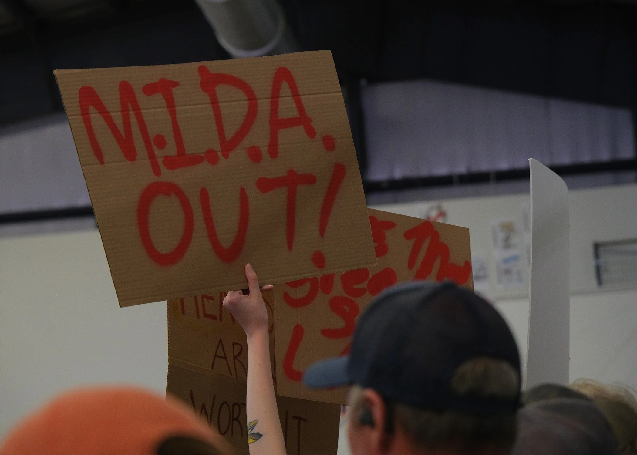 An attendee holds up a sign reading  “M.I.D.A. OUT!” In protest of the Military Installment Development Authority and its role in the Stratos Project. 